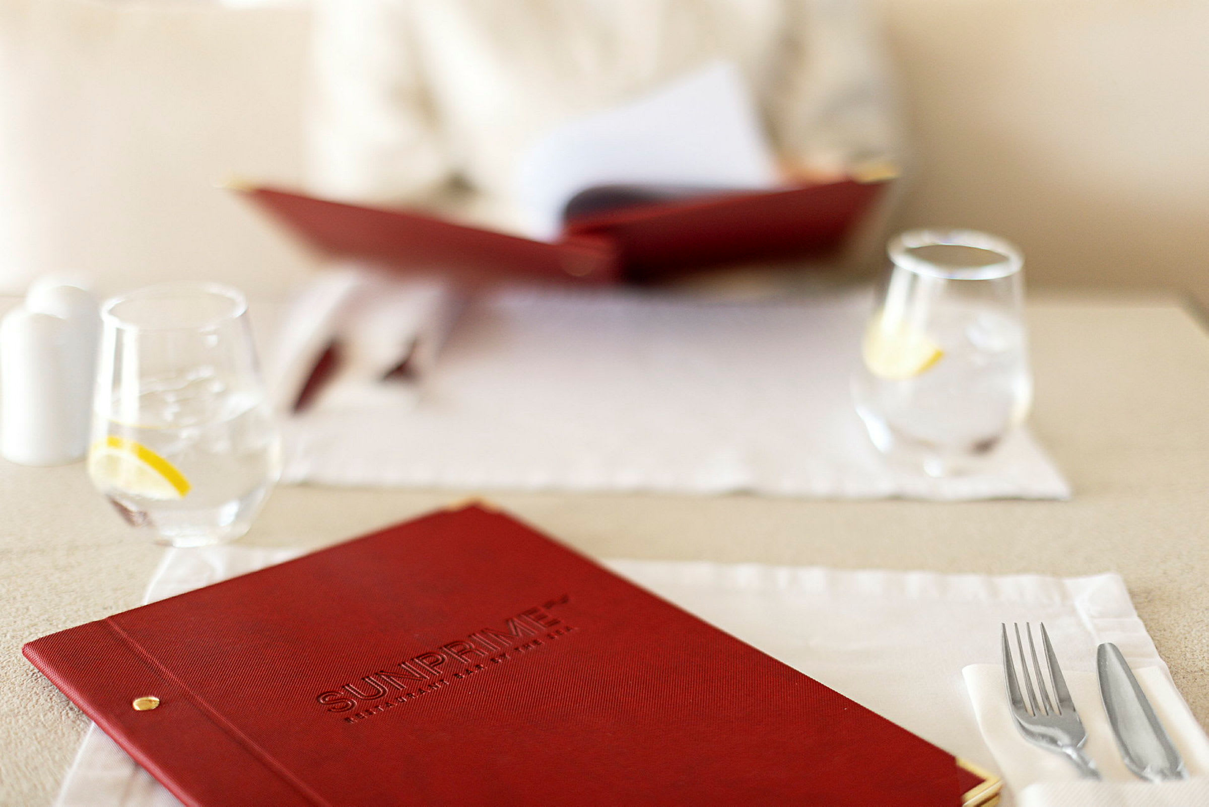 Nærbilde av en rød menybok på et dekket restaurantbord med glass og bestikk. (AI-generert tekst)
