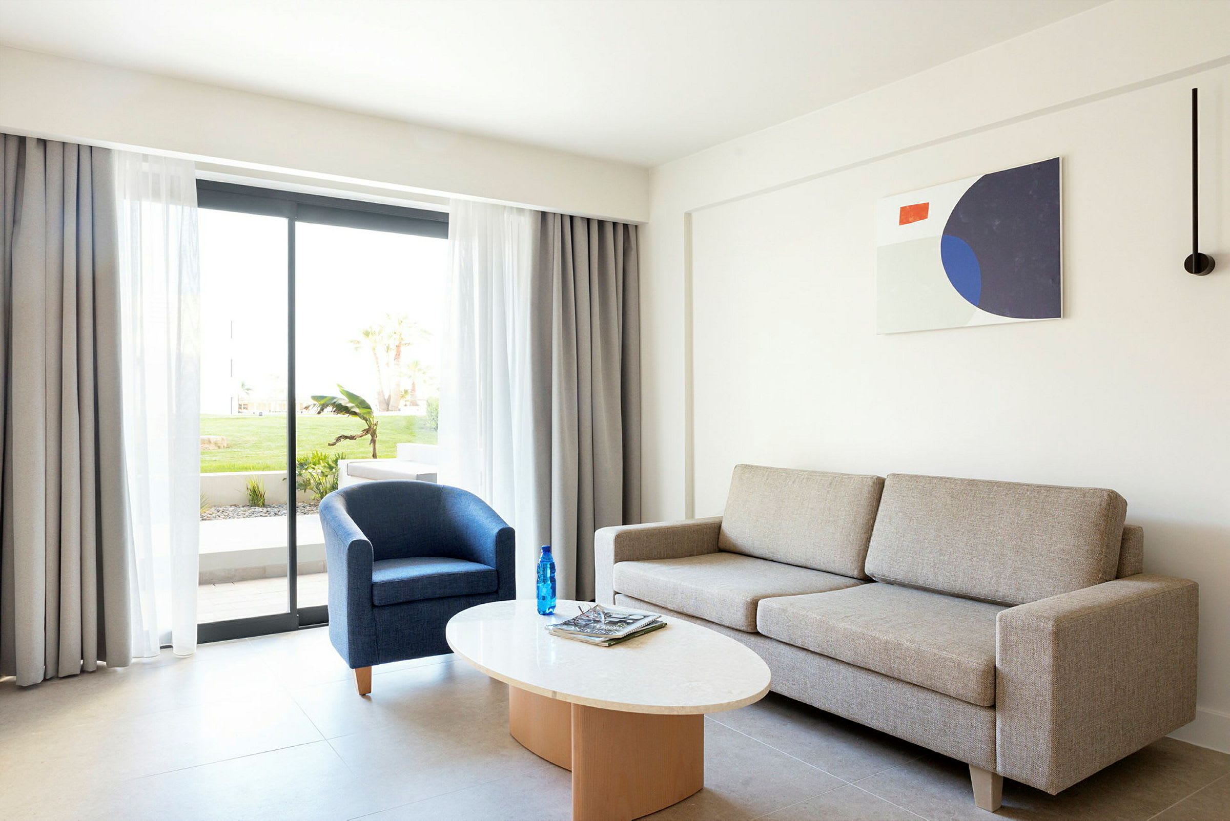 Moderne og lyst oppholdsrom med sofa, lenestol og et salongbord. Glassdør til uteområde med grøntområder. (AI-generert tekst)
