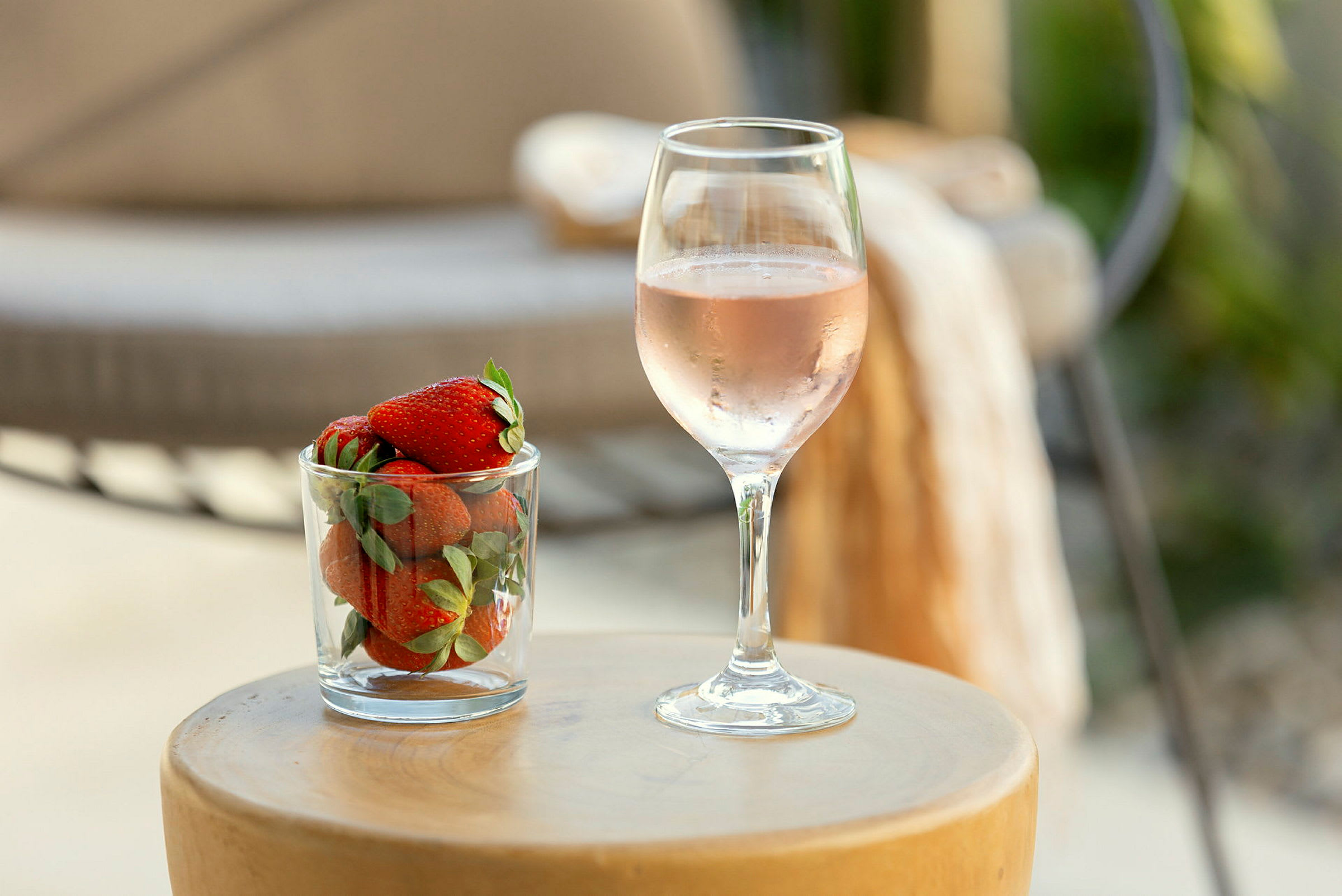 Et glass med jordbær ved siden av et glass rosévin står på et rundt bord. (AI-generert tekst)