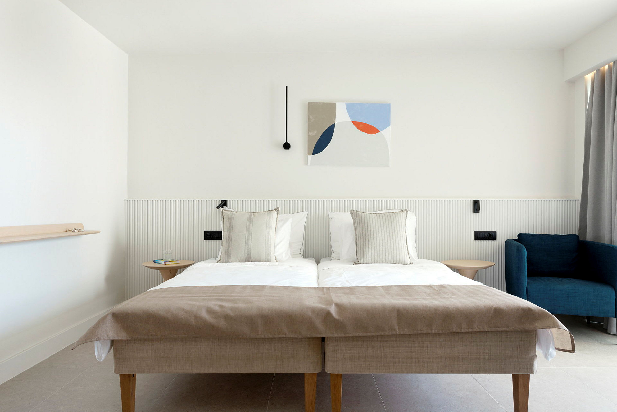 Et hotellrom med en dobbeltseng, en blå lenestol og moderne veggdekor. (AI-generert tekst)