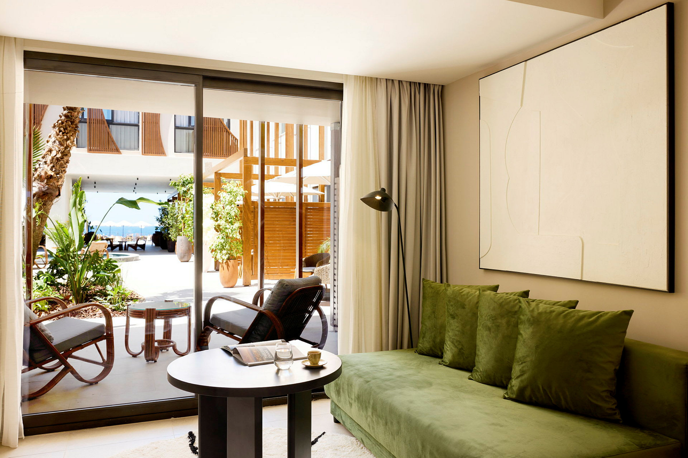 Et oppholdsrom med en grønn sofa og et rundt bord ved siden av store glassdører som fører ut til en terrasse. (AI-generert tekst)