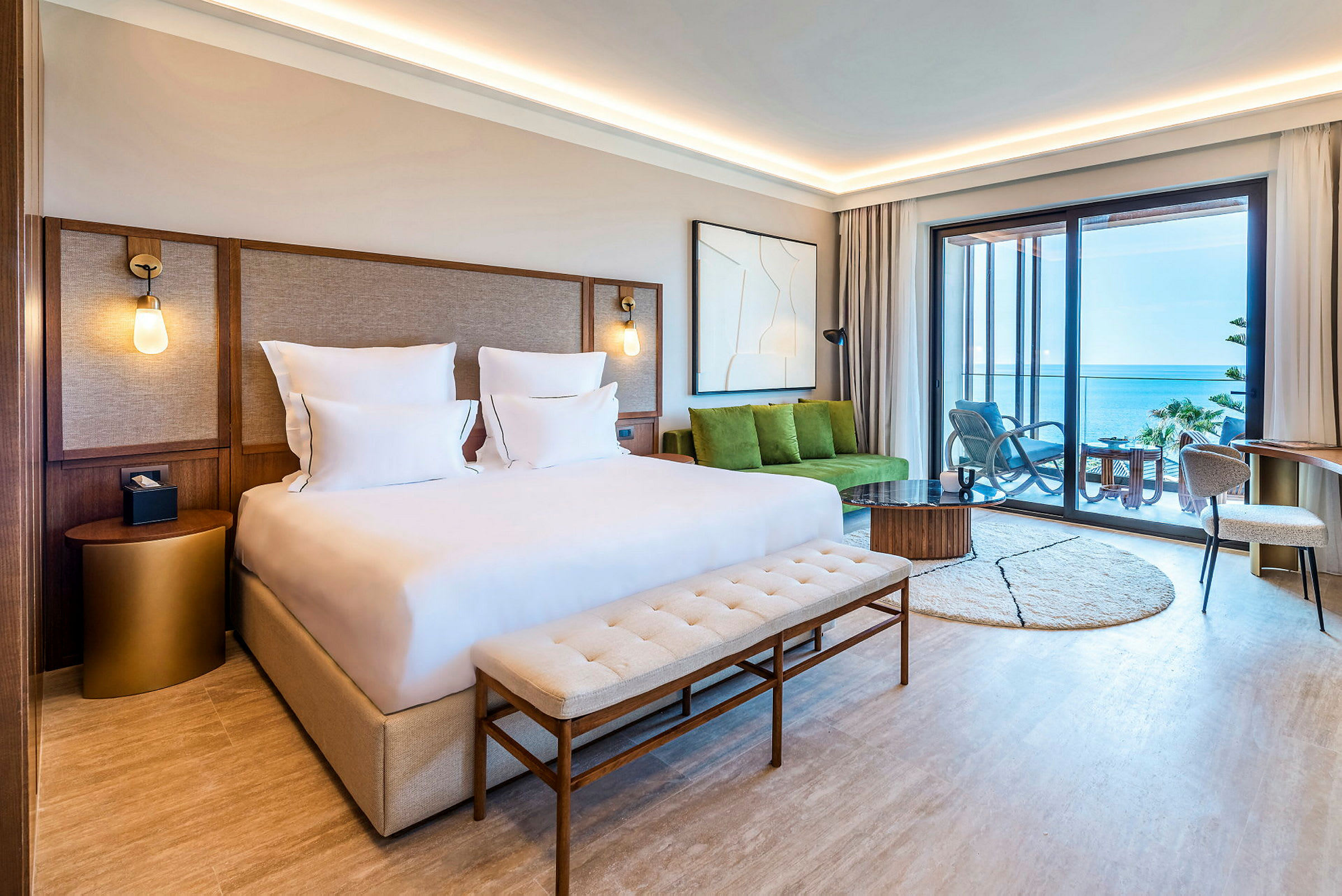 Et moderne hotellrom med en dobbeltseng og utsikt over havet fra en møblert balkong. (AI-generert tekst)