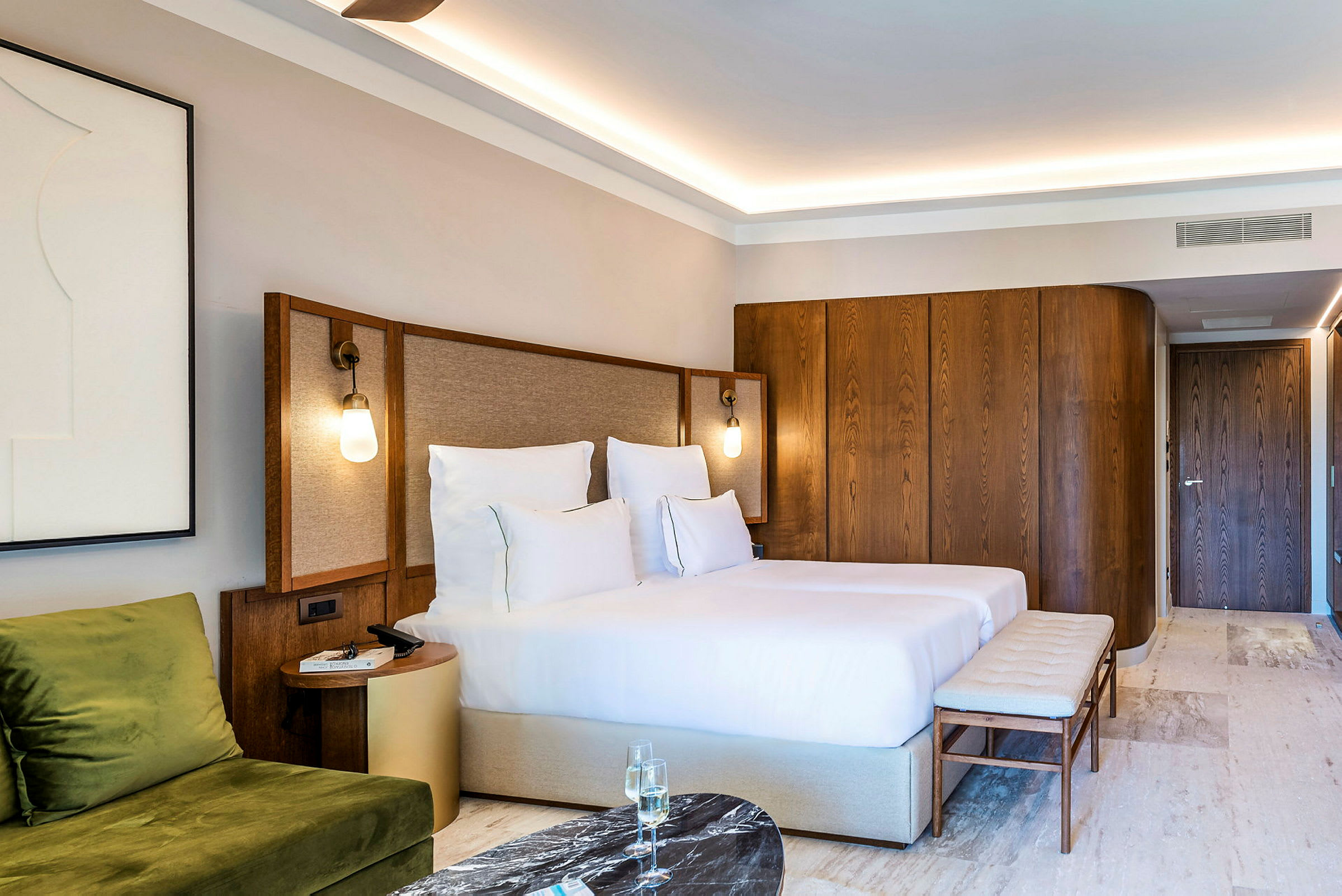 Hotellrom med en dobbeltseng, en sitteplass med grønn sofa, et sidebord og innredning i tre. (AI-generert tekst)