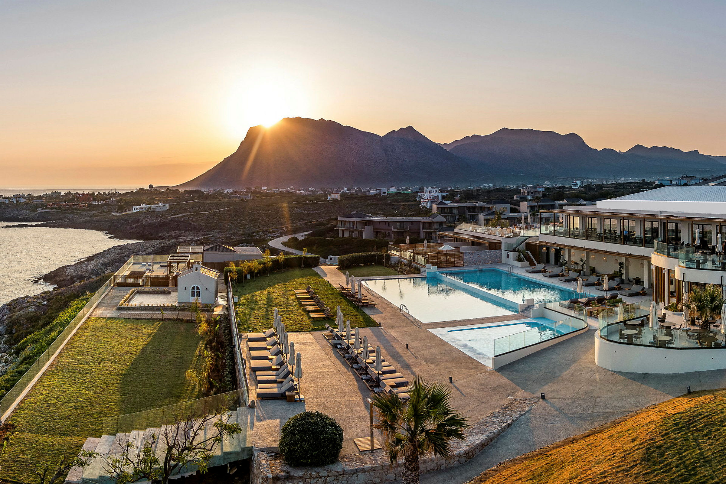 Solnedgang over hotellområde med basseng, grøntområder og omkringliggende fjellandskap. (AI-generert tekst)