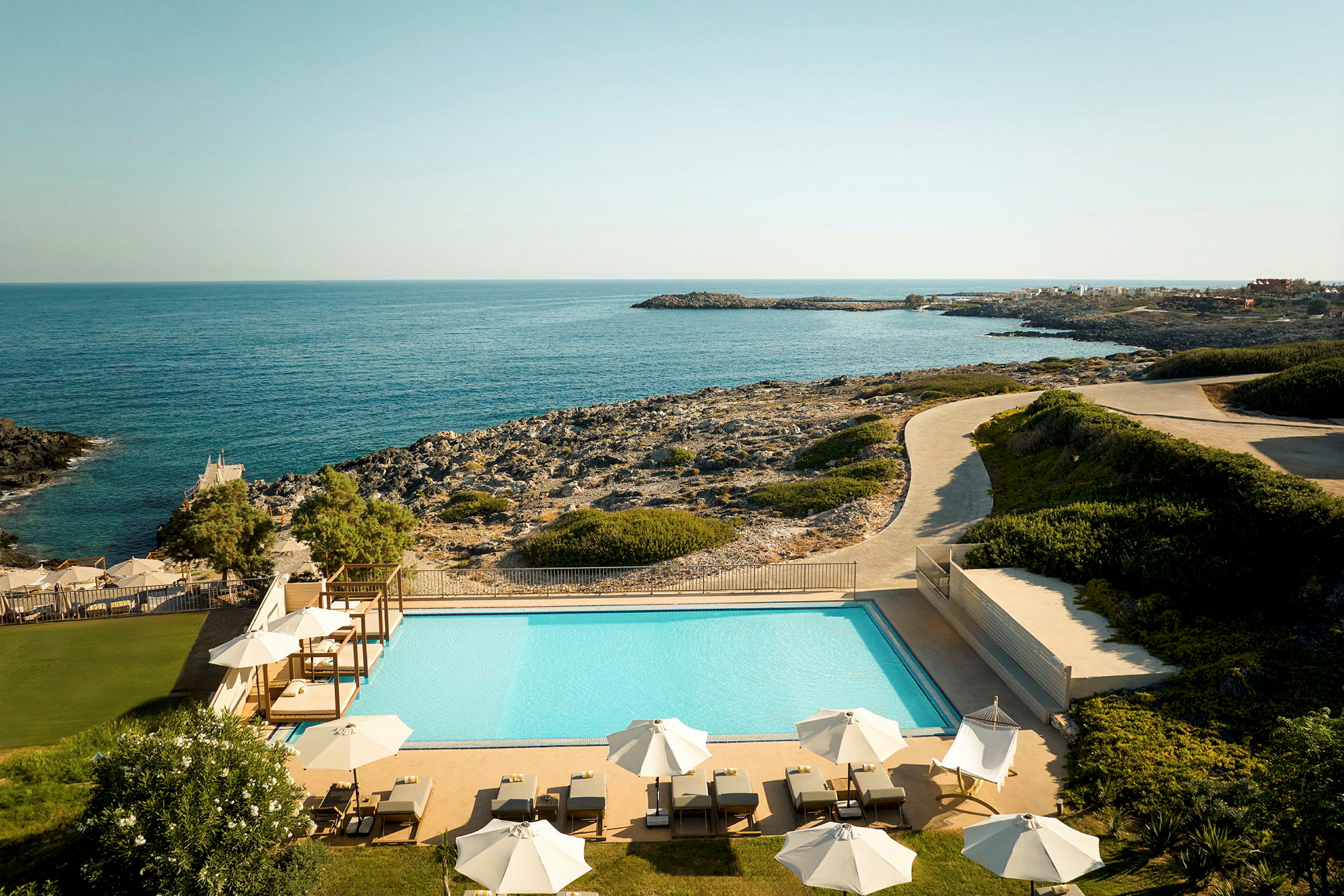 Hotellområde med utendørsbasseng og solsenger, utsikt over havet og klipper. (AI-generert tekst)