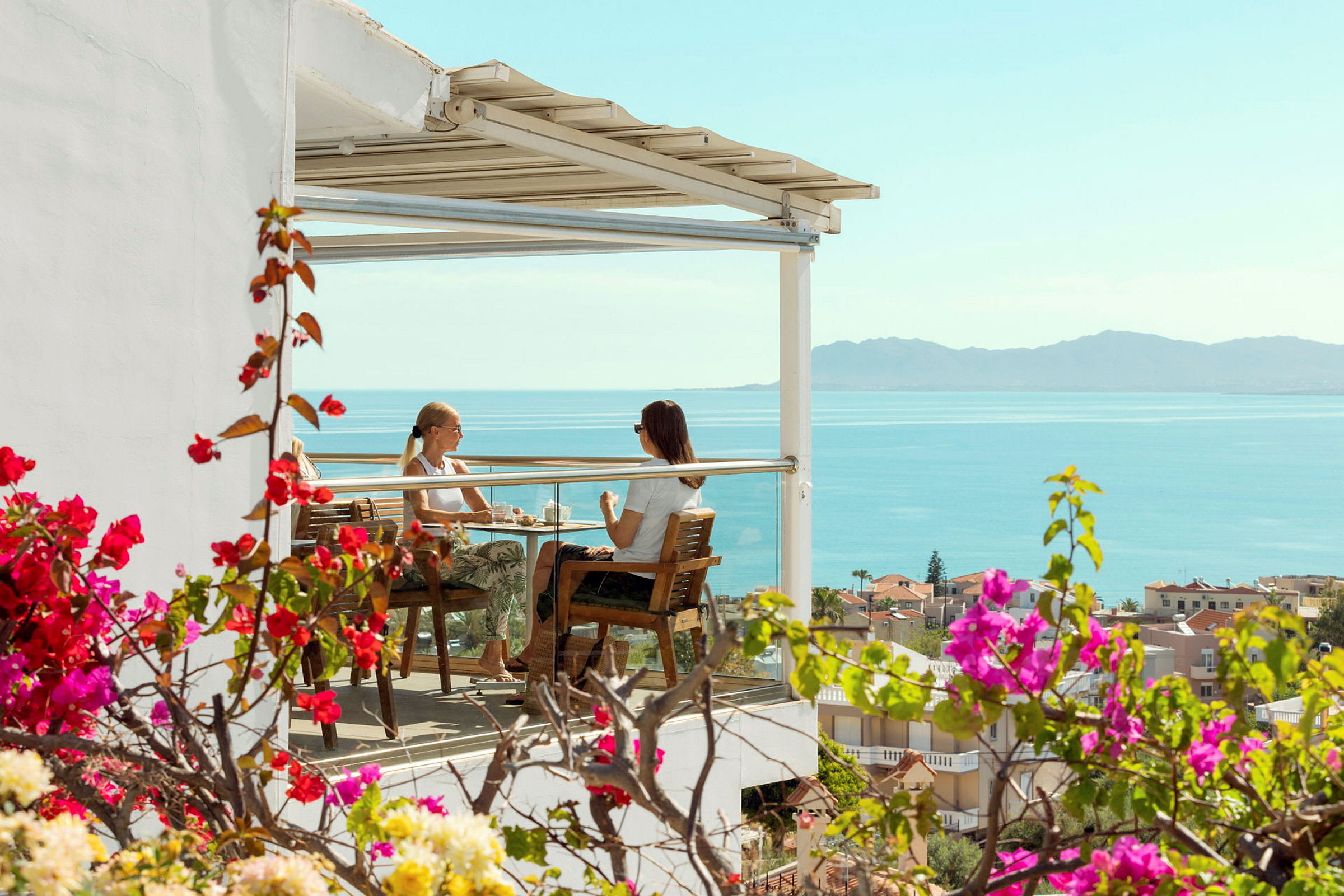 To personer sitter på en terrasse med utsikt over havet. (AI-generert tekst)