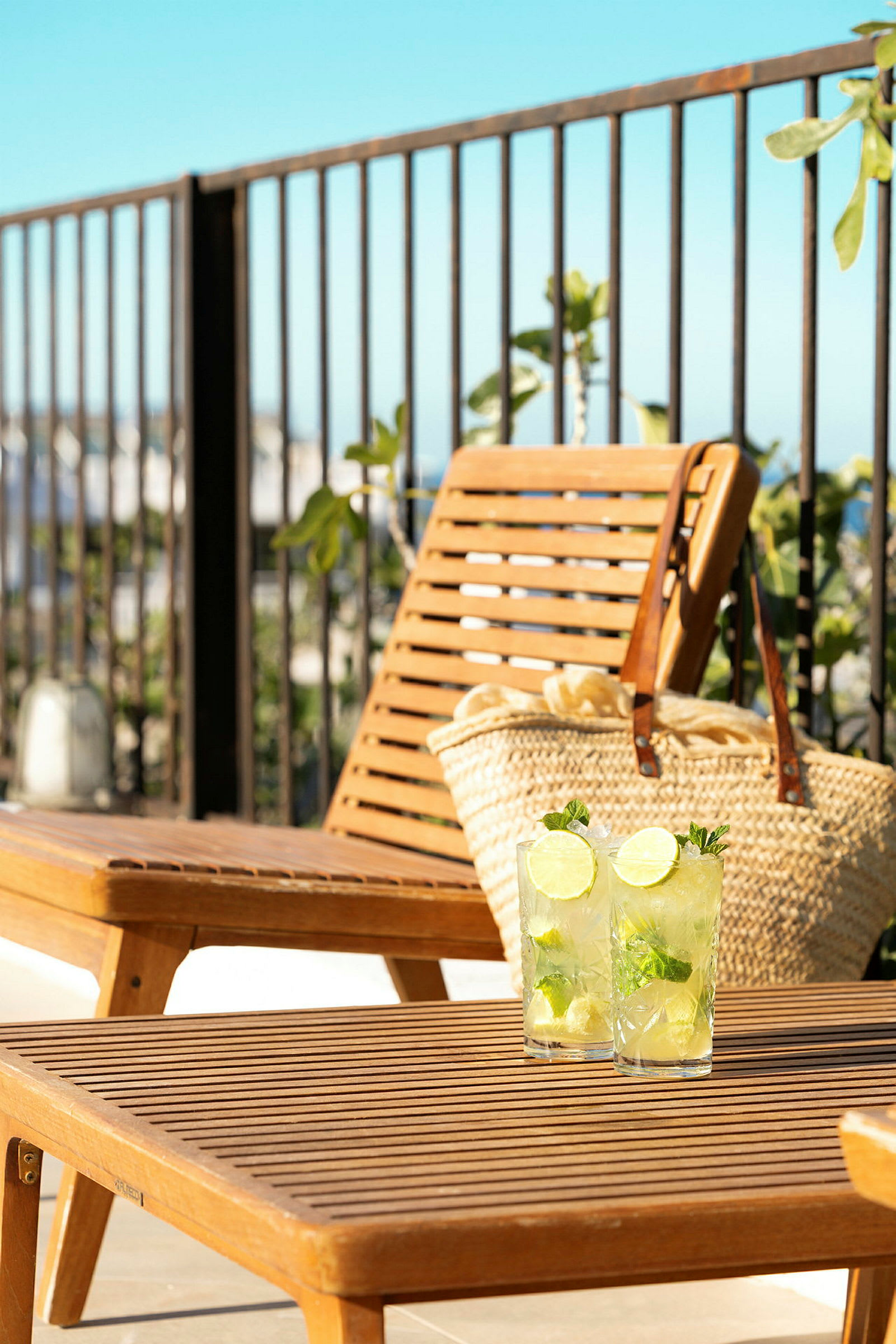 To glass med lime- og myntedrikk på et bord av tre foran en solseng og en strandveske. (AI-generert tekst)