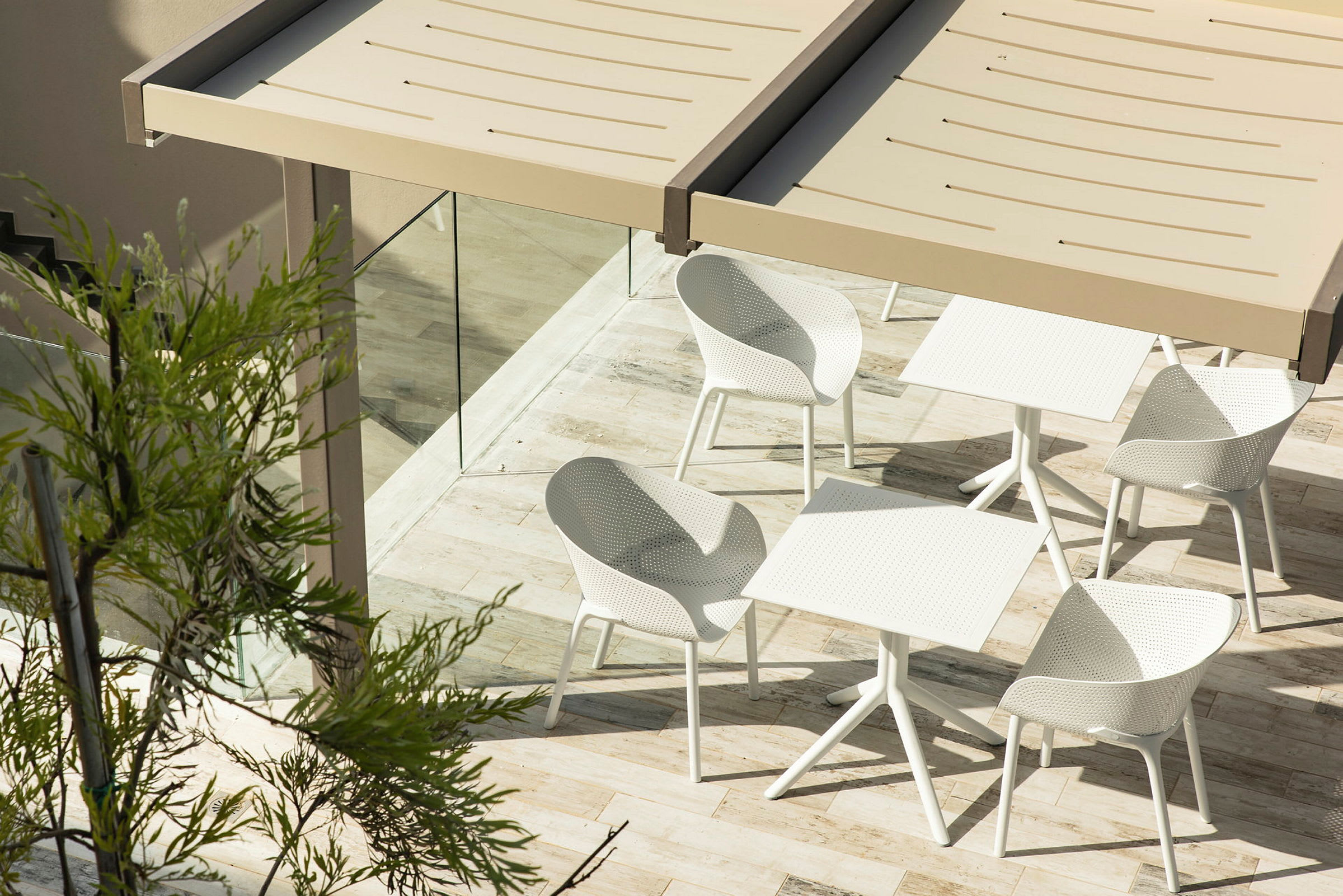 Utendørsområde med bord og stoler under et tak, omgitt av glass og planter. (AI-generert tekst)