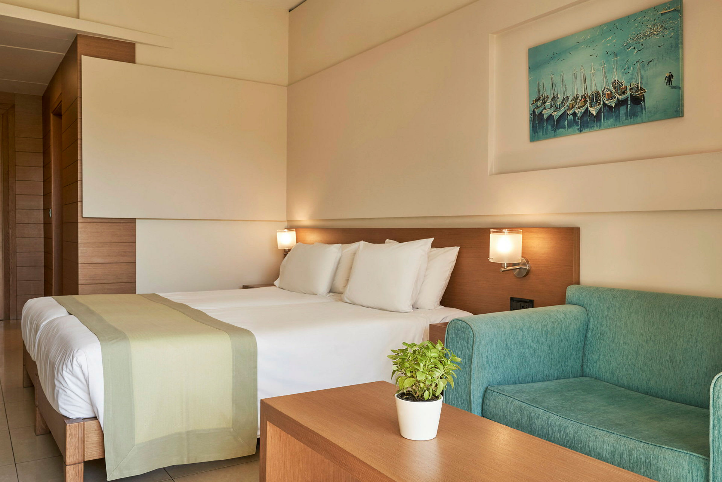 Et hotellrom med en dobbeltseng, grønn sofa og veggkunst. (AI-generert tekst)