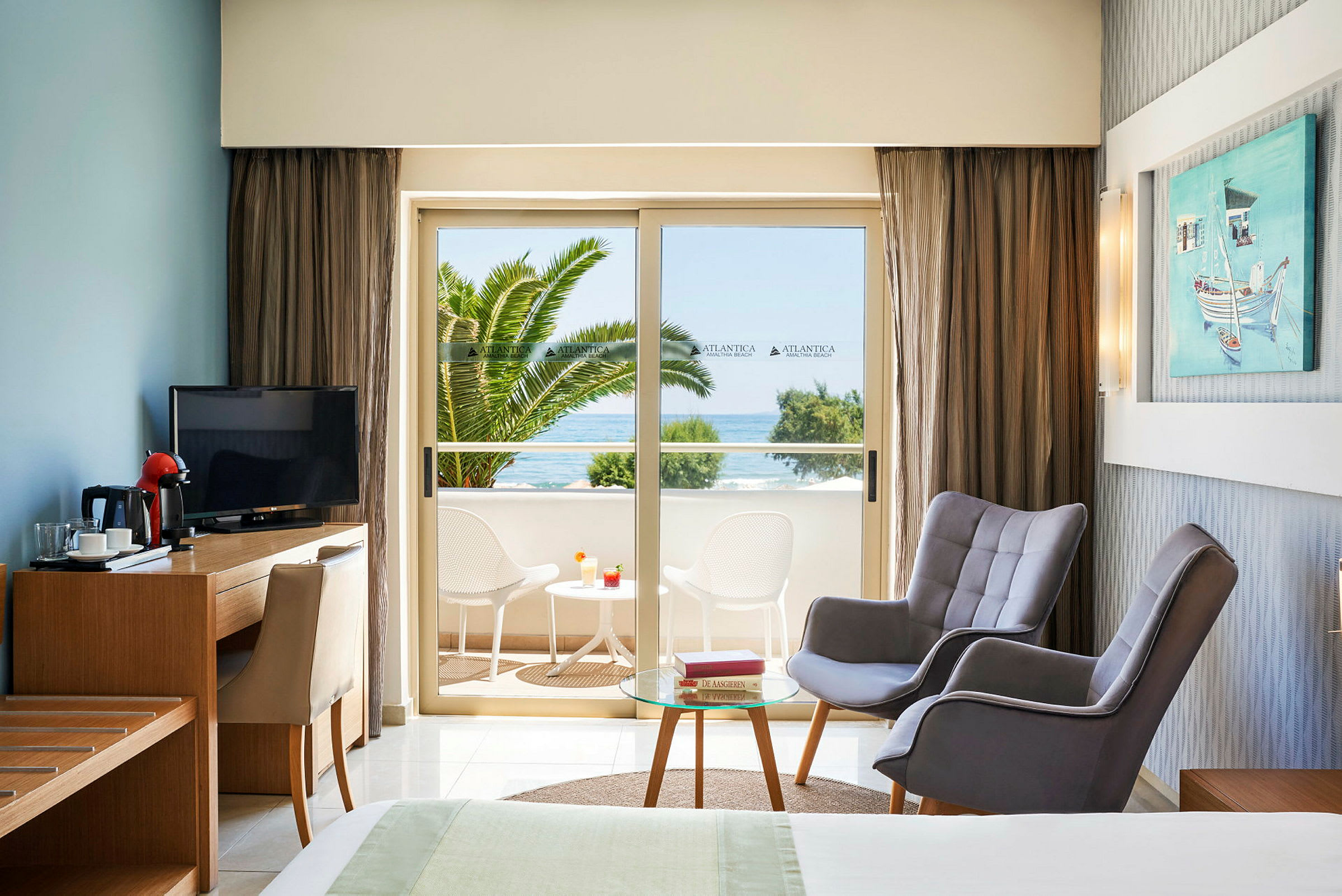 Hotellrom med sittegruppe og utsikt mot balkong med bord og stoler samt havutsikt. (AI-generert tekst)