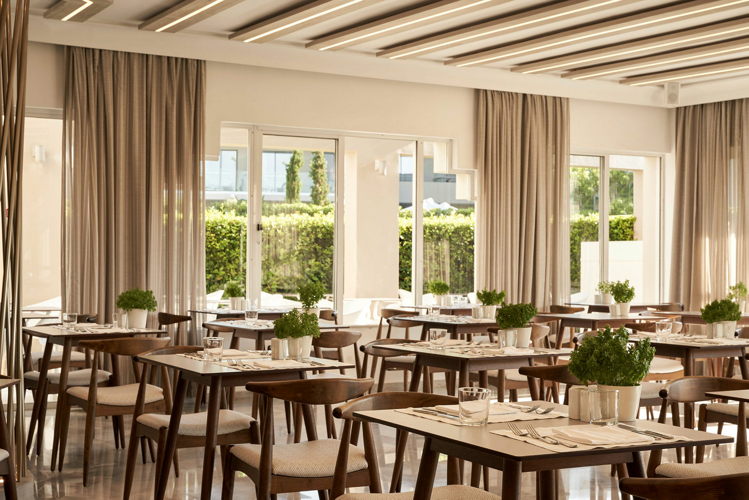 Et moderne innredet restaurantområde med bord og stoler i tre samt urtepotter. (AI-generert tekst)