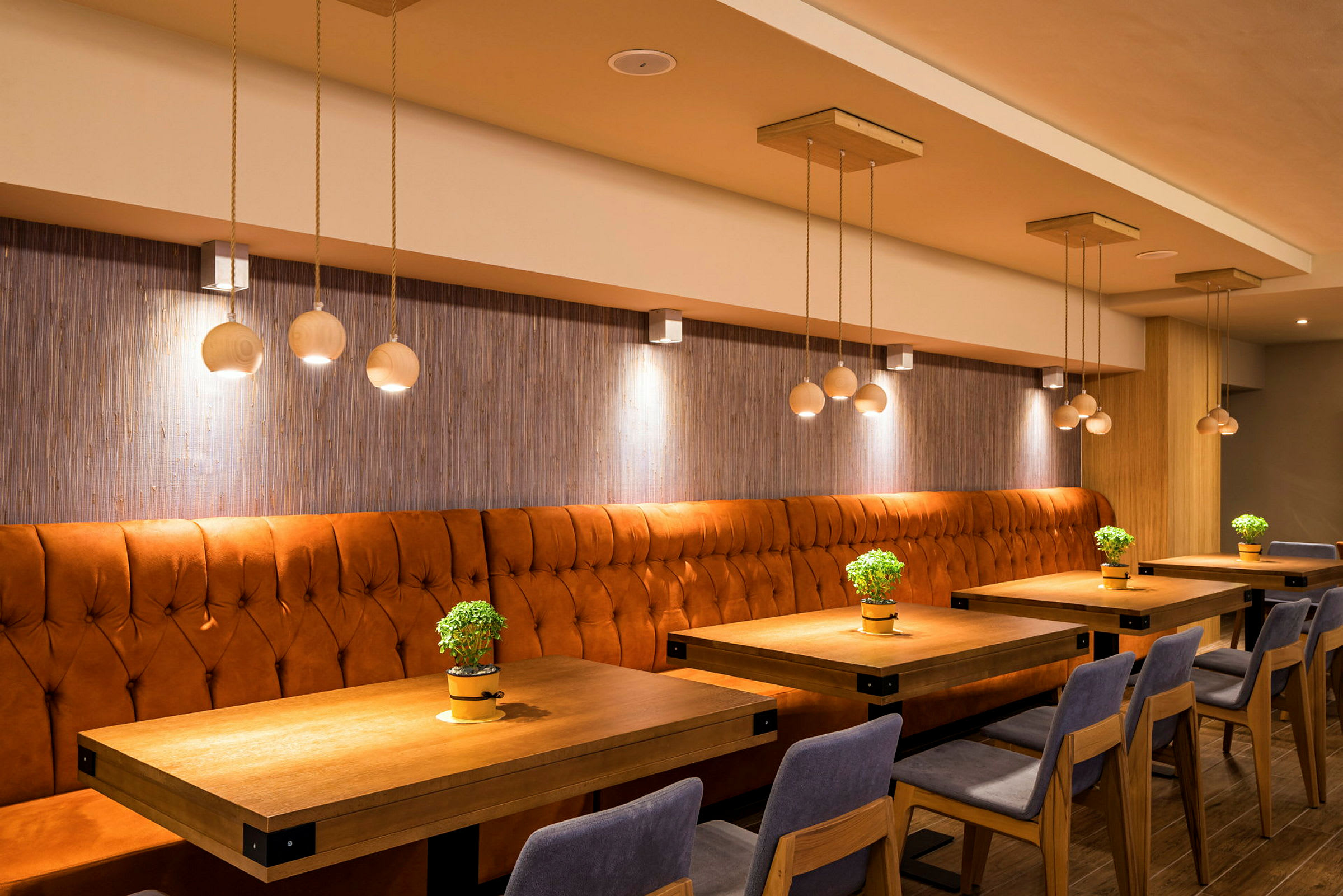 Interiør av en restaurant med oransje polstrede benker og bord dekorert med små grønne planter. (AI-generert tekst)