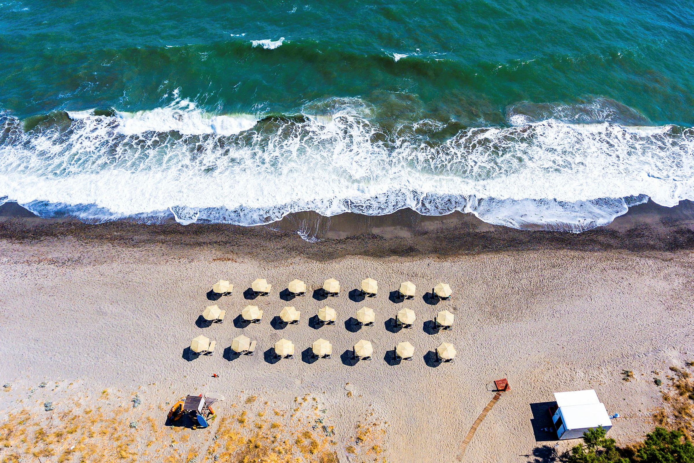 Flyfoto av en strand med parasoller og bølger. (AI-generert tekst)