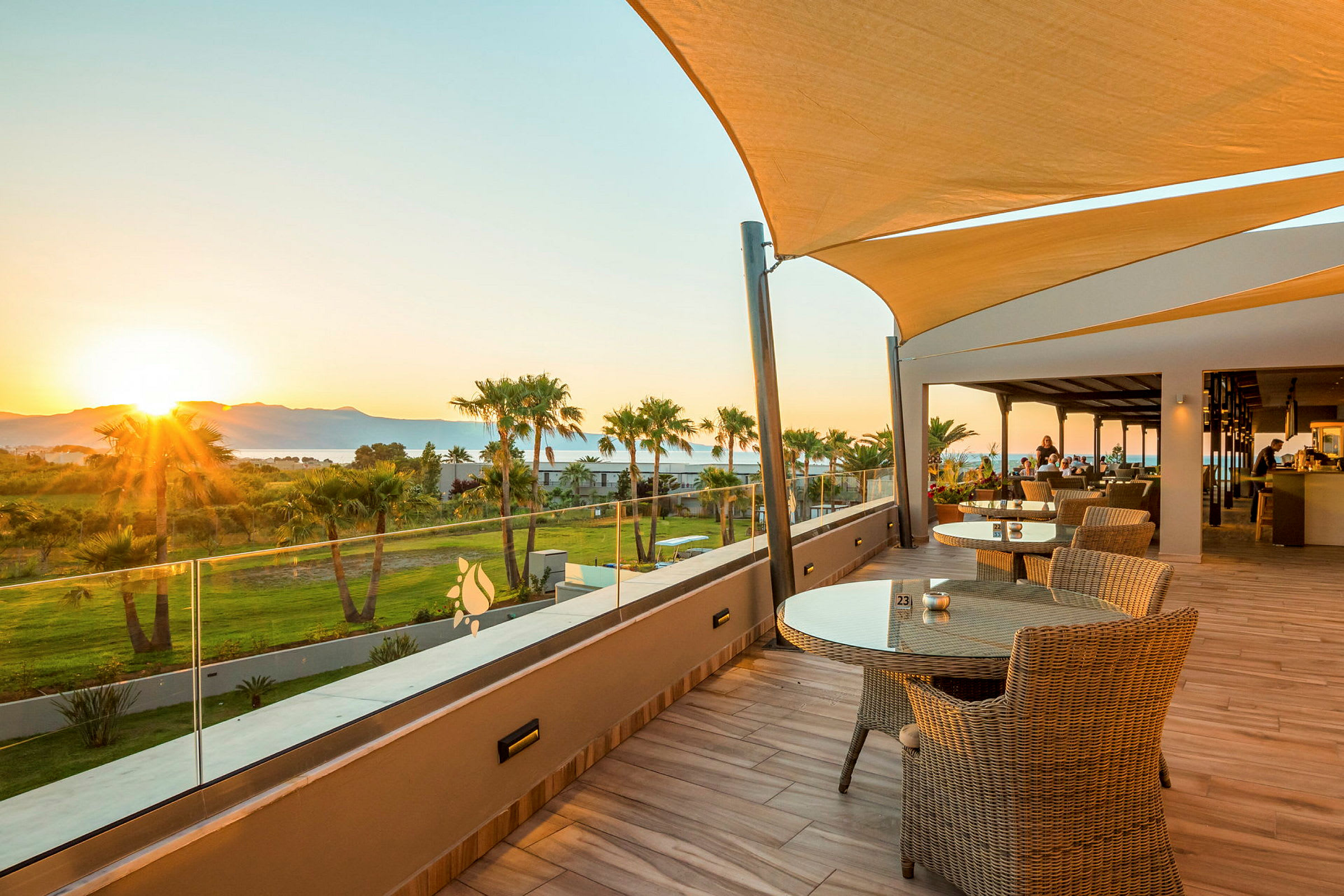 Terrasse med bord og stoler samt utsikt over grøntområde og solnedgang. (AI-generert tekst)
