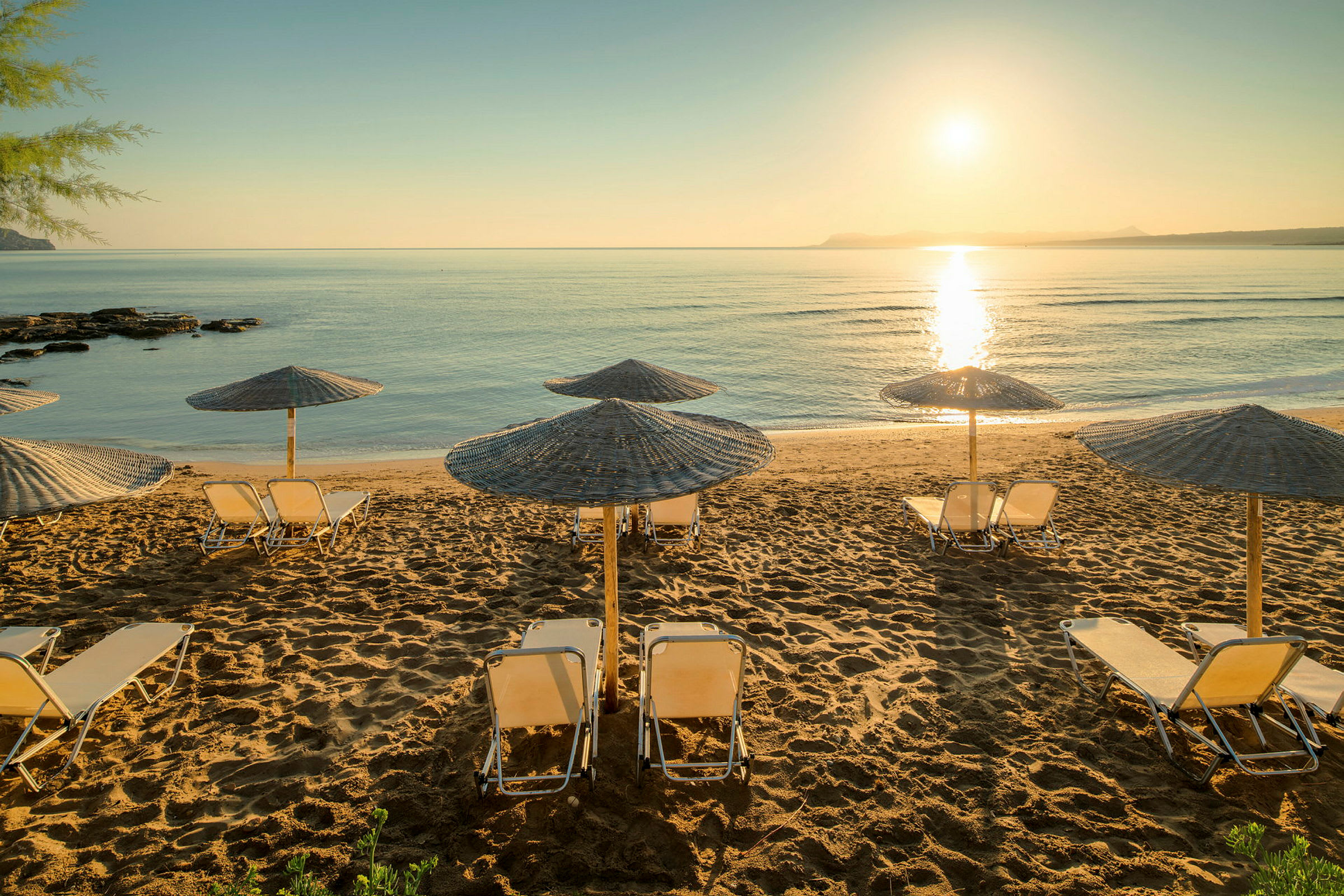 Strand med solparasoller og solsenger ved solnedgang. (AI-generert tekst)