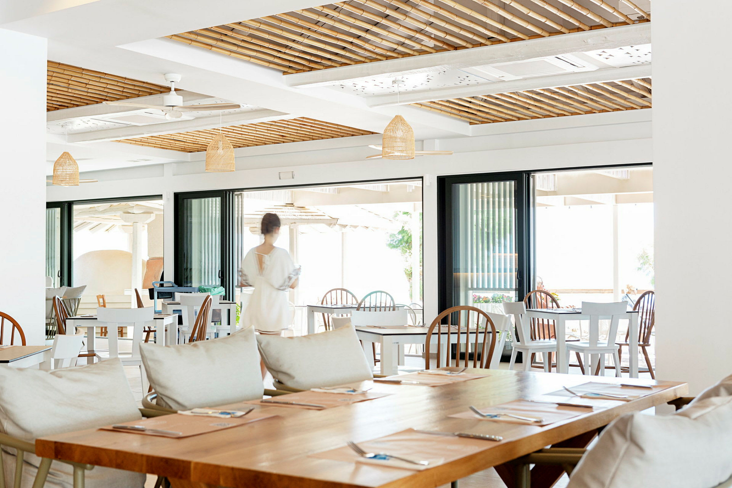 Bildet viser en restaurantmiljø med tomme bord, stoler og en person i bevegelse i bakgrunnen. (AI-generert tekst)