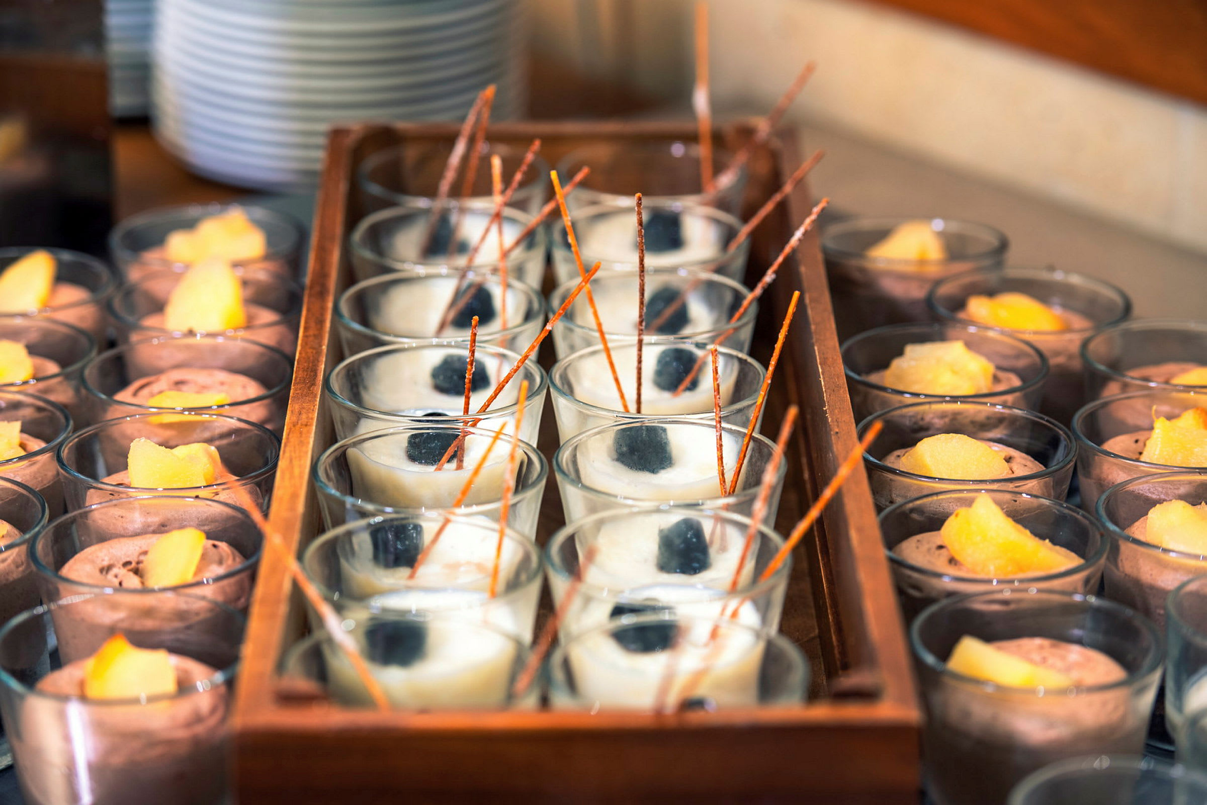 Flere glass med dessert, både lyse og mørke varianter, dekorert med fruktbiter og sjokoladesticks. (AI-generert tekst)