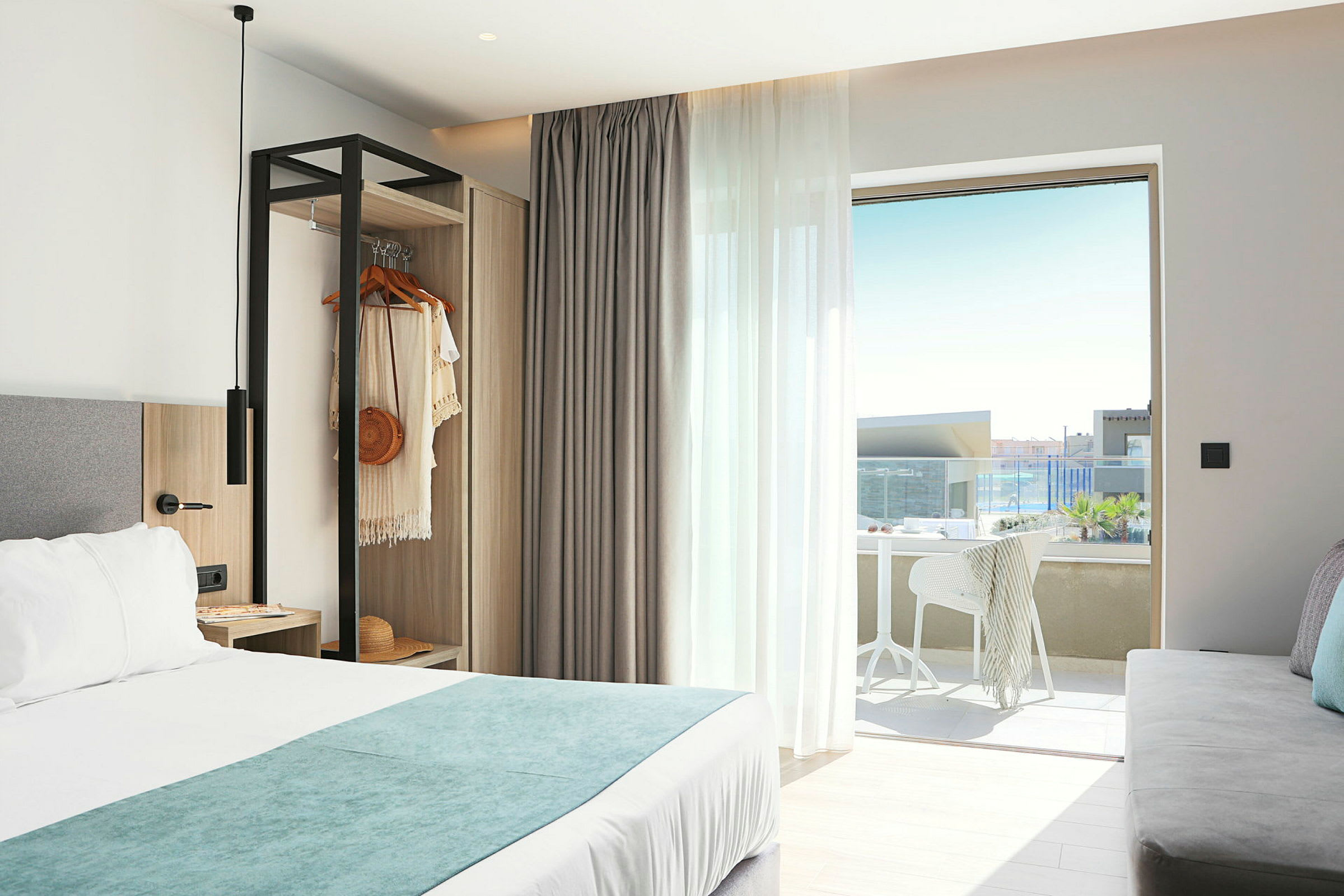 Et hotellrom med en dobbeltseng, en åpen garderobe og en møblert balkong med utsikt. (AI-generert tekst)