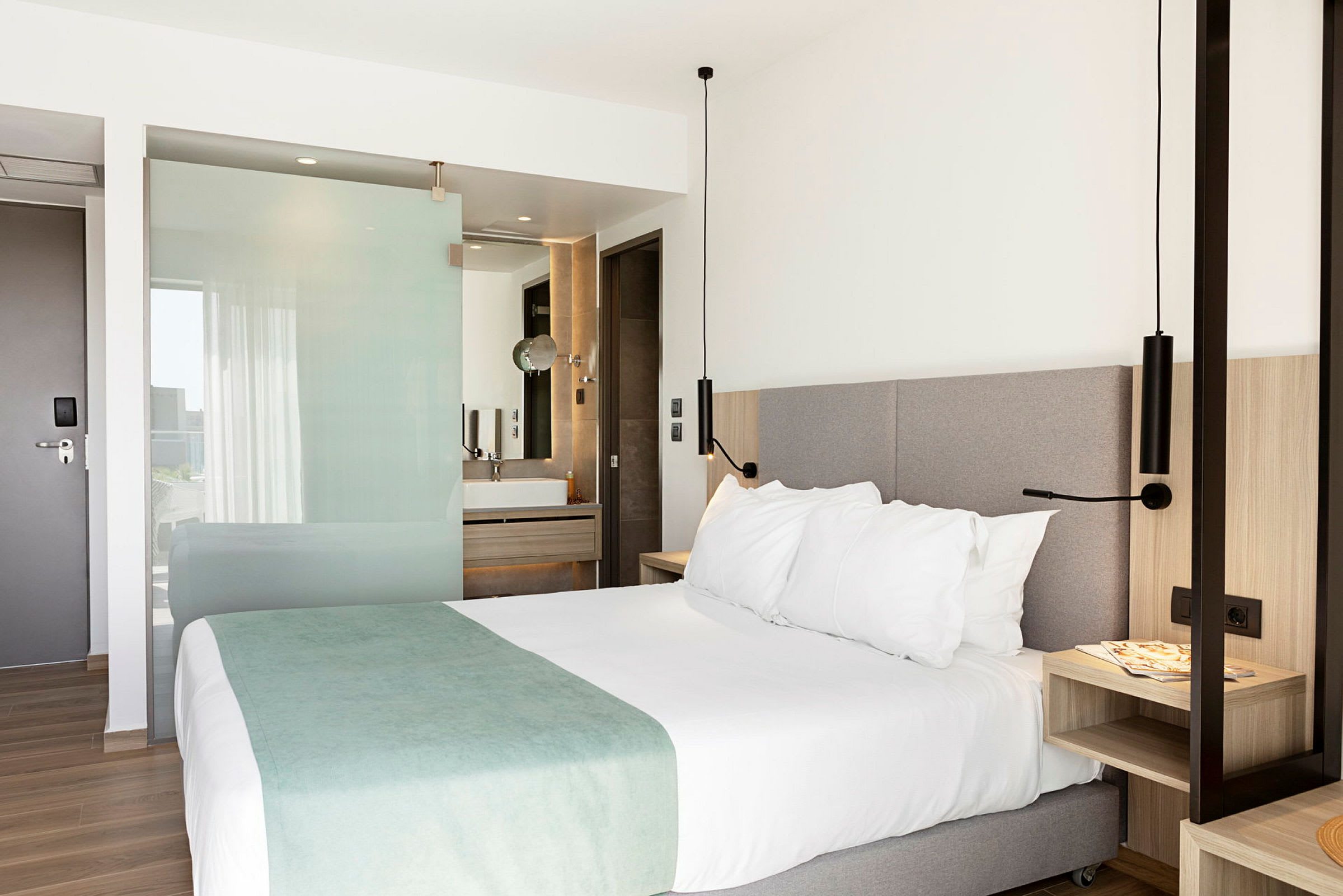 Hotellrom med en dobbeltseng, nattbord og åpen planløsning mot bad. (AI-generert tekst)