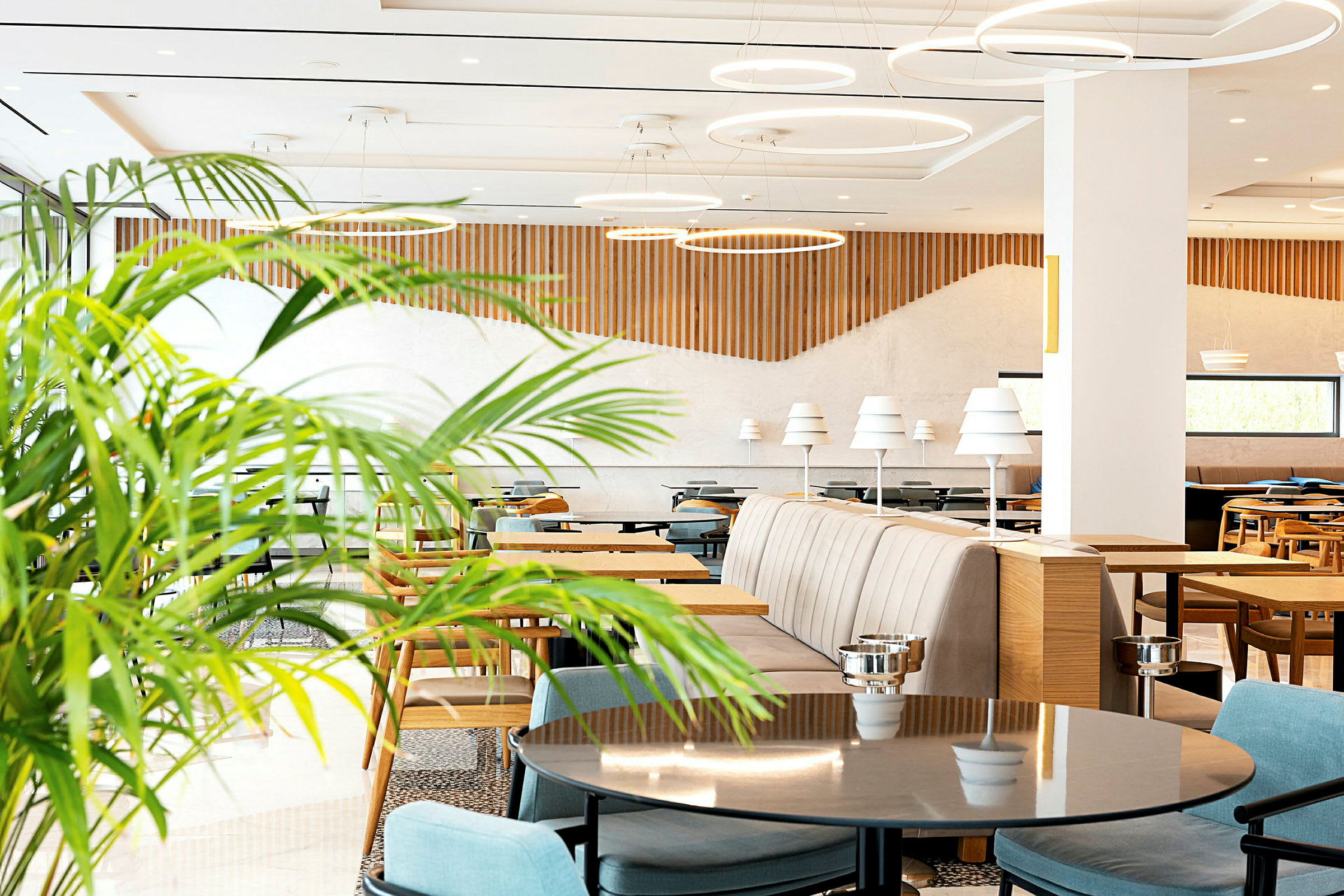 Lyst og moderne restaurant med bord, stoler og dekorative grønne planter. (AI-generert tekst)