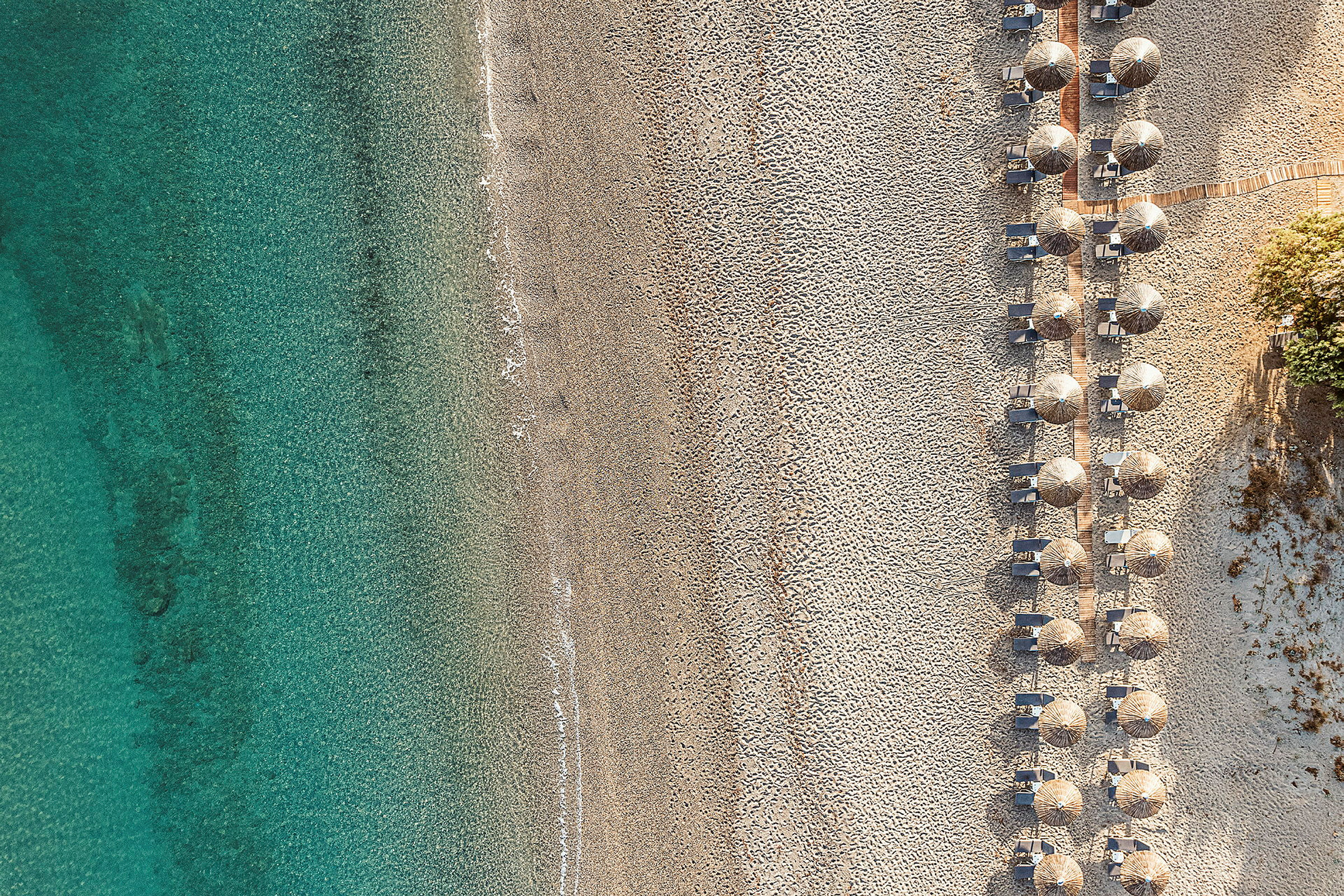 Luftfoto av steinstrand med parasoller og solsenger på rekke. (AI-generert tekst)