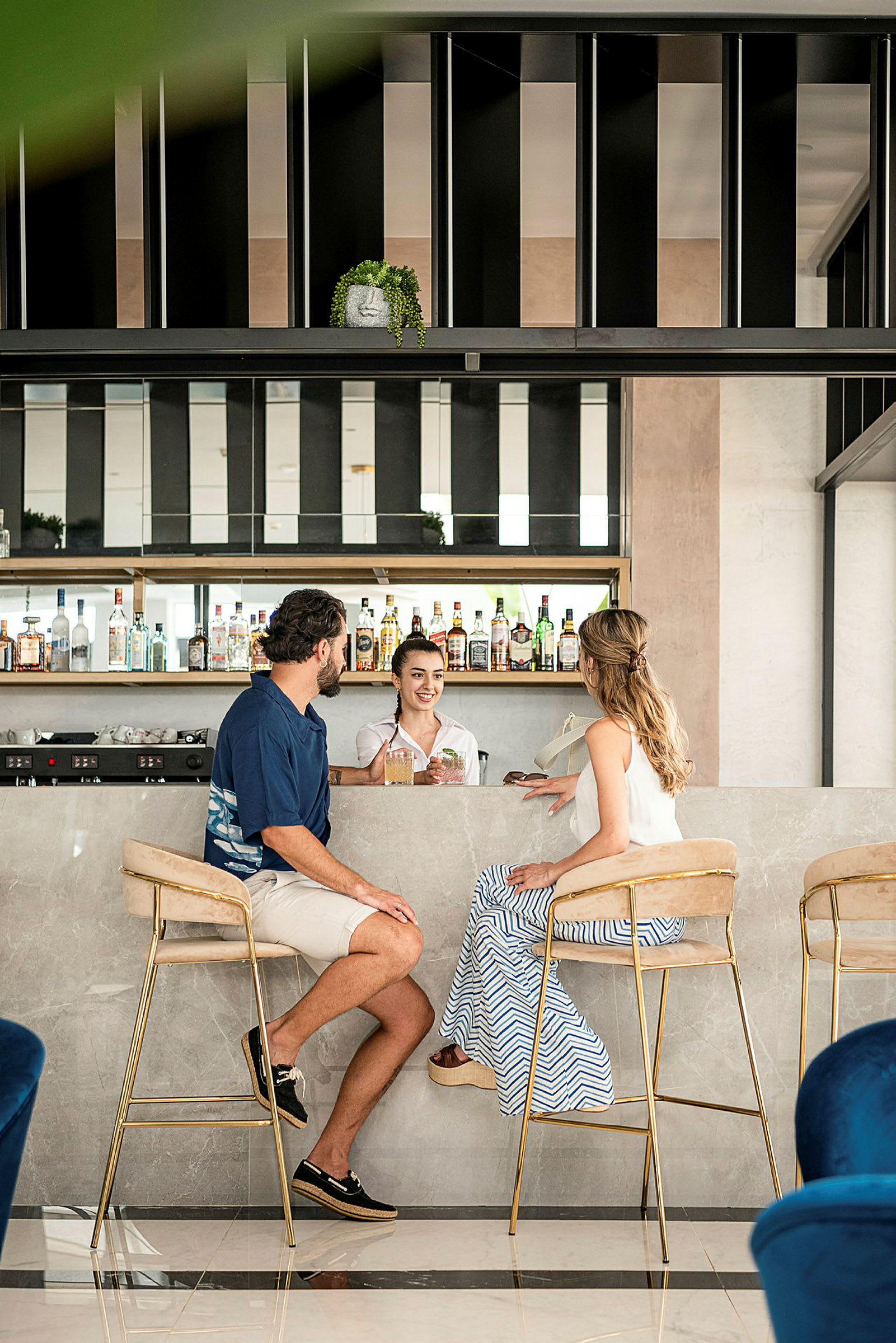 Bilde av to personer sittende ved en marmordisk på en moderne bar med hyller fulle av flasker. (AI-generert tekst)