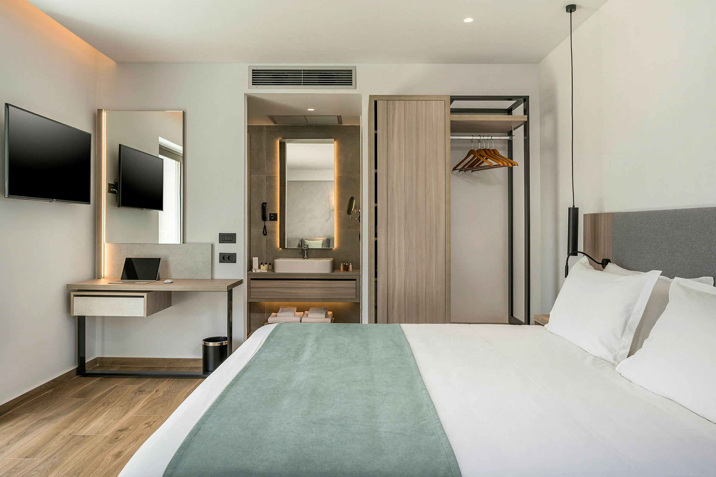 Moderne hotellrom med dobbeltseng, skrivebord med TV samt en åpen garderobe og bad. (AI-generert tekst)