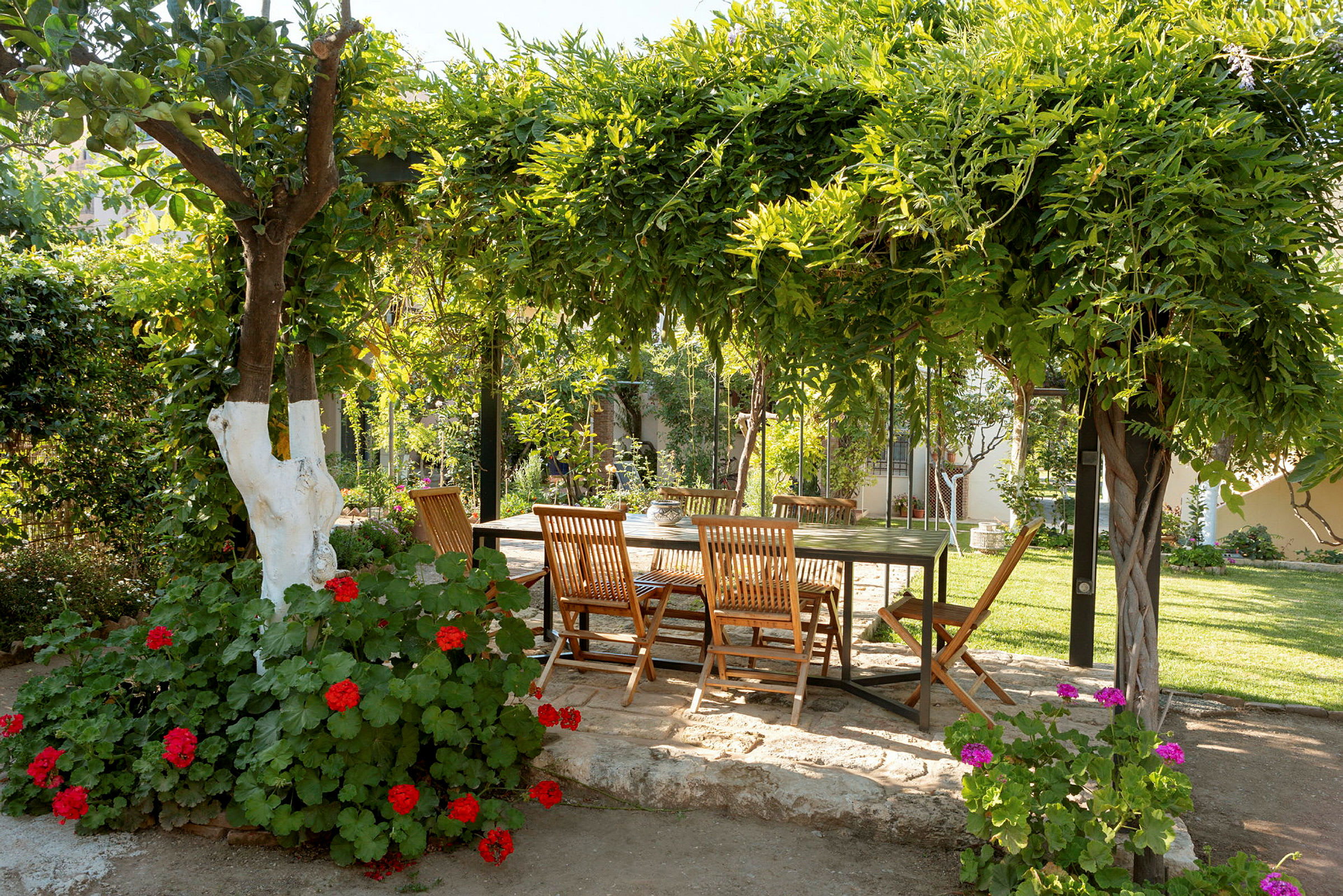 Hage med et bord og stoler under en frodig pergola. (AI-generert tekst)