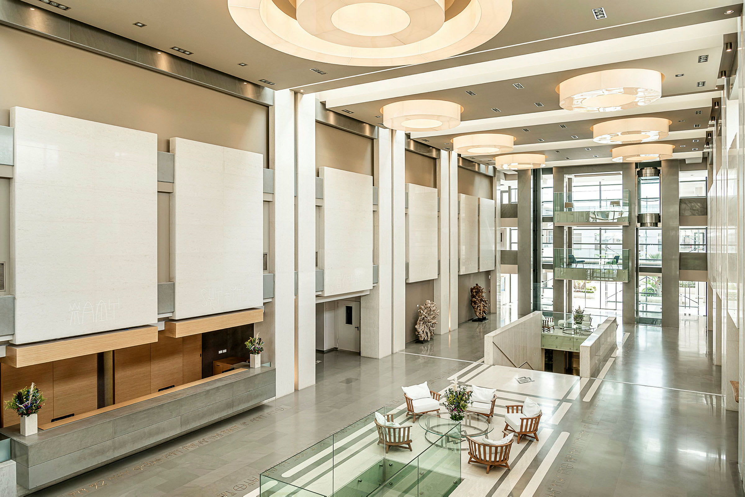 En lys og romslig lobby med moderne interiørdetaljer, glassrekkverk og sittegrupper ved et bord. (AI-generert tekst)