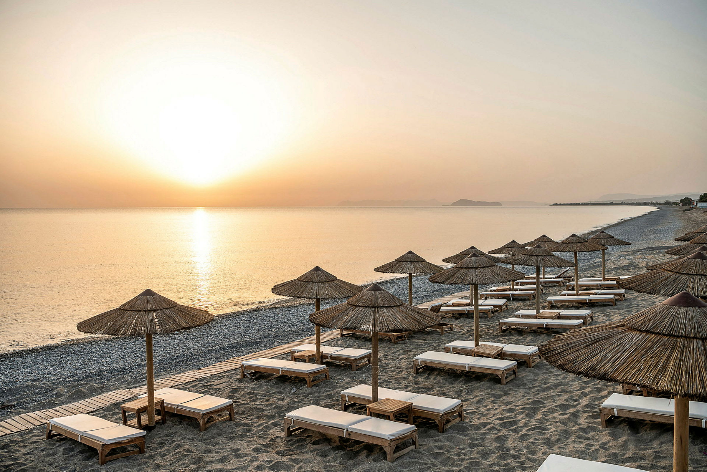 Strand ved solnedgang med parasoller og solsenger. (AI-generert tekst)