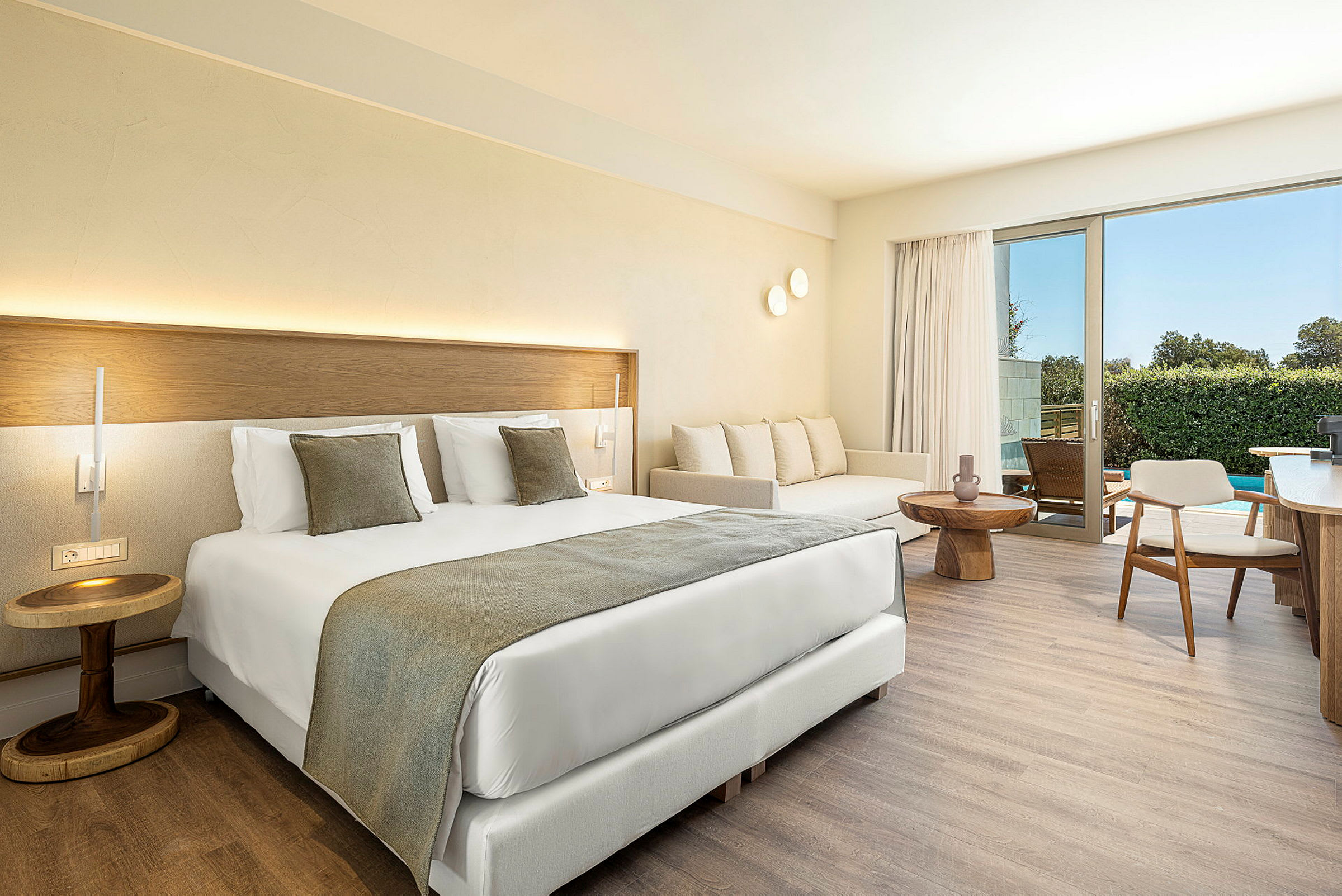 Et moderne hotellrom med en stor seng, sofa og et bord. Rommet har lyse vegger og en balkong med utsikt. (AI-generert tekst)
