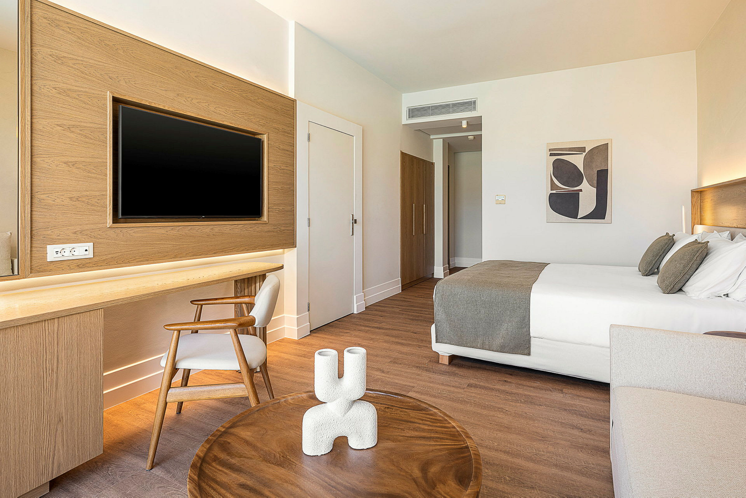 Et moderne hotellrom med en dobbeltseng, et skrivebord med stol og en TV på veggen. Et lite bord er i forgrunnen. (AI-generert tekst)