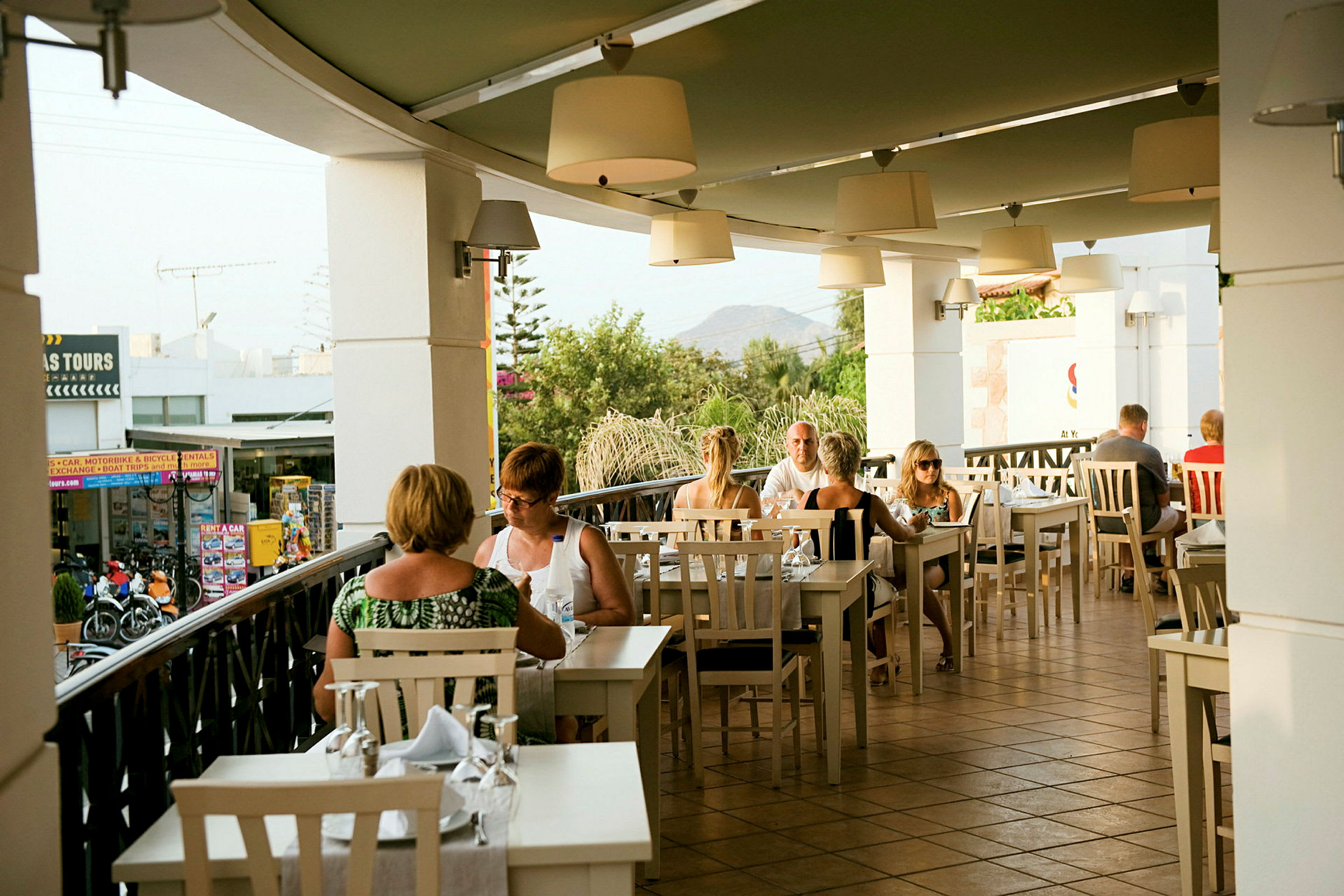 En utendørs restaurant med folk som sitter ved bord. (AI-generert tekst)