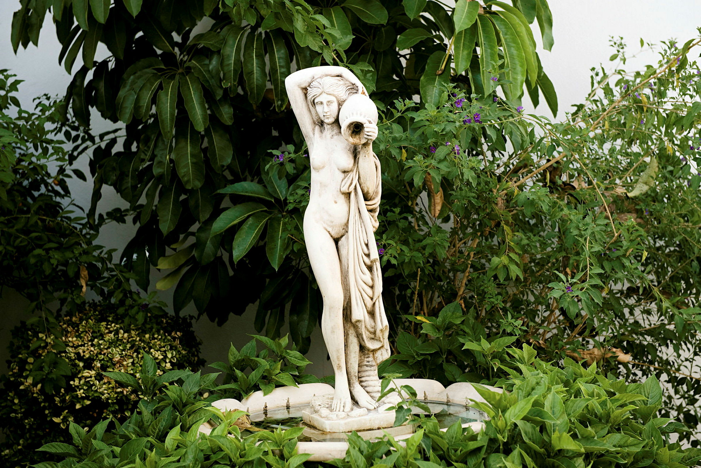 Statue av en stående person omgitt av grønne planter. (AI-generert tekst)