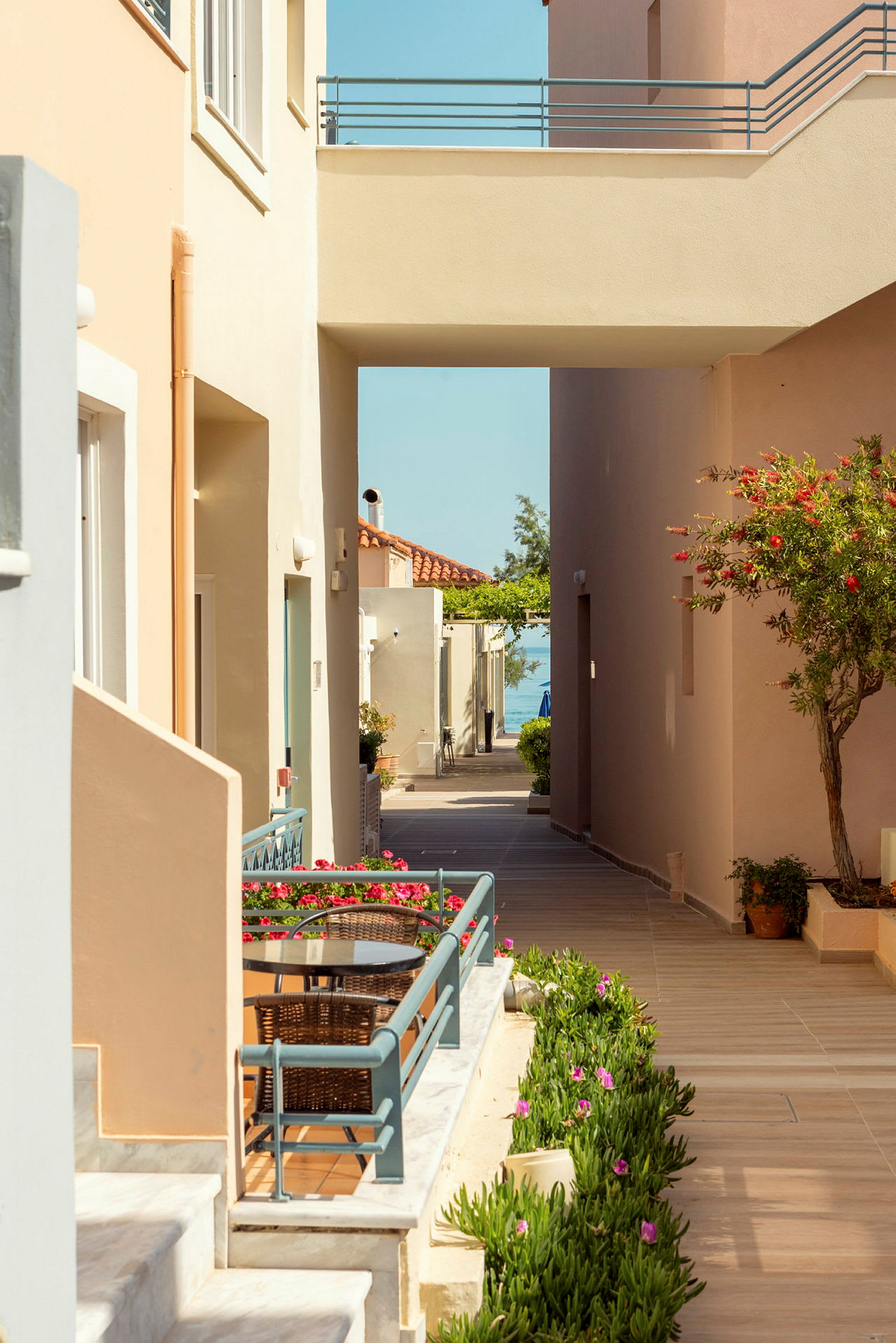 Bilde som viser en gangvei mellom bygninger med blomsterdekorasjoner og en liten terrasse i forgrunnen. (AI-generert tekst)