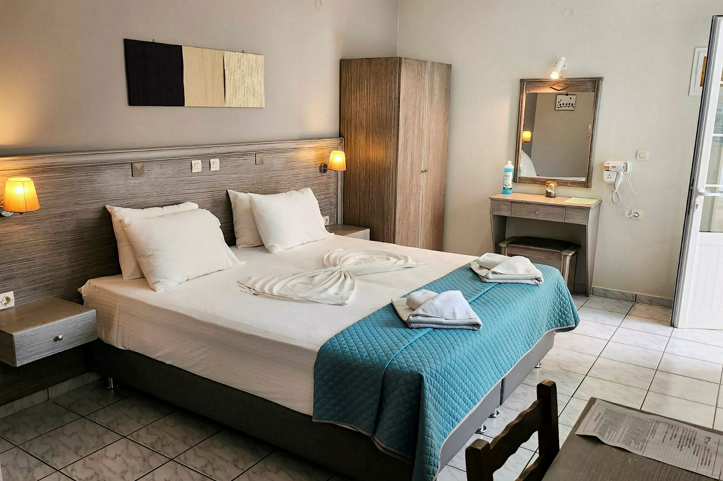 Hotellrom med en dobbeltseng, garderobe, sminkbord og lyse tekstiler. (AI-generert tekst)