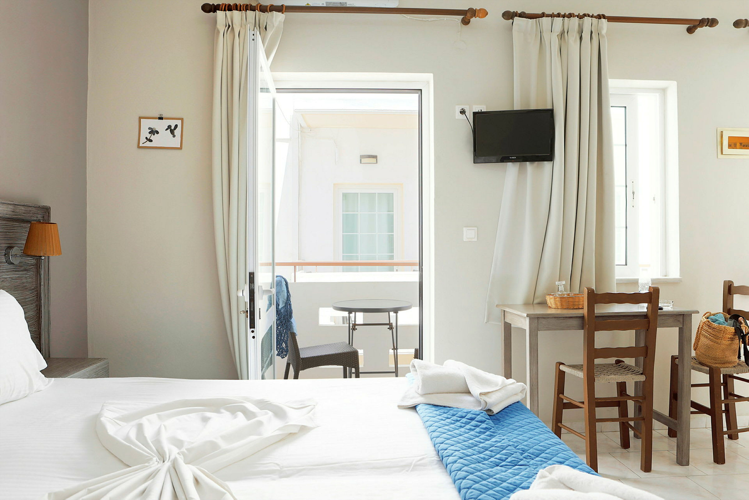 Interiør av et hotellrom med en dobbeltseng, et bord med to stoler og en balkong med utsikt. (AI-generert tekst)