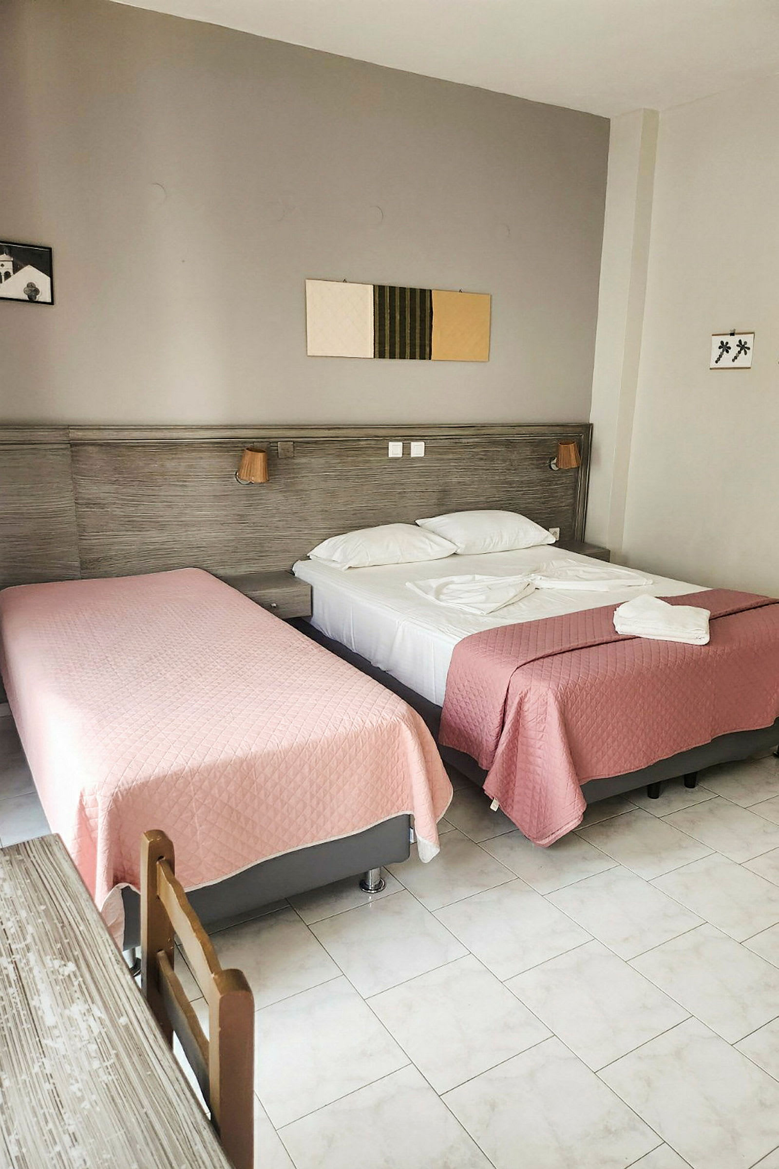 Et hotellrom med to senger oppredde med rosa sengetepper. (AI-generert tekst)