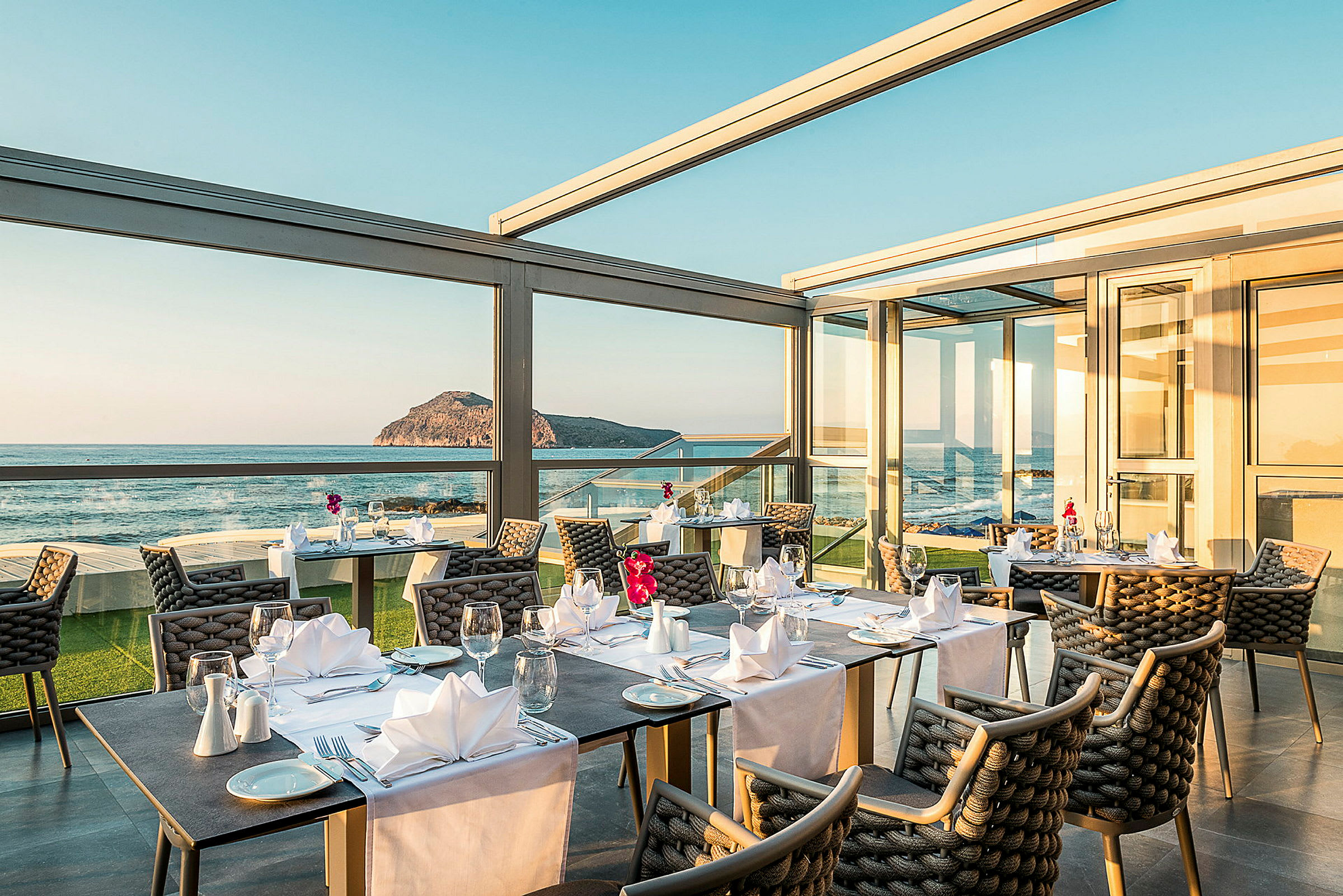 Restaurant med bord som er dekket og stor vindusutsikt mot hav og landskap. (AI-generert tekst)