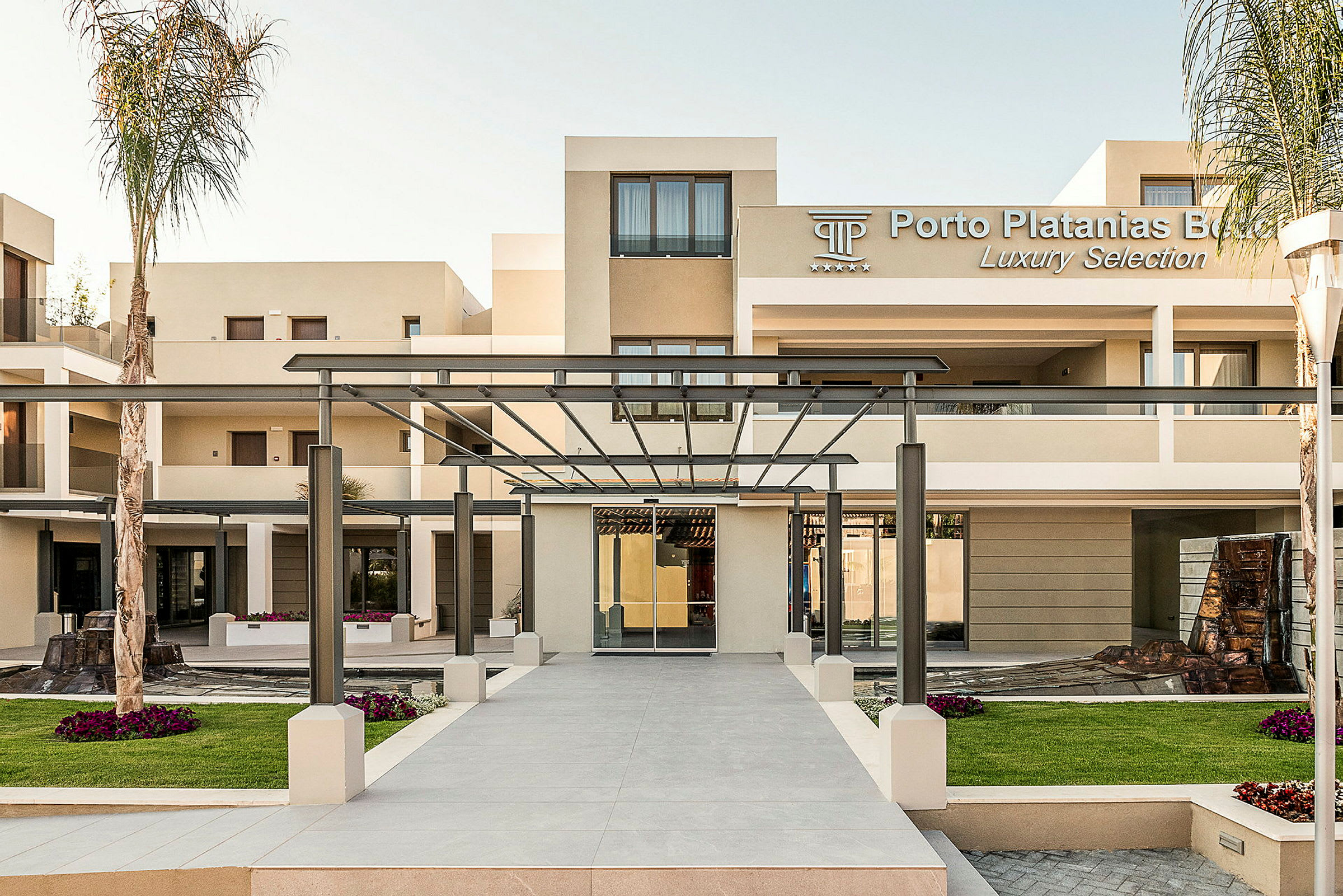 Inngang til Porto Platanias Beach Resort med moderne bygninger og en pergola. (AI-generert tekst)
