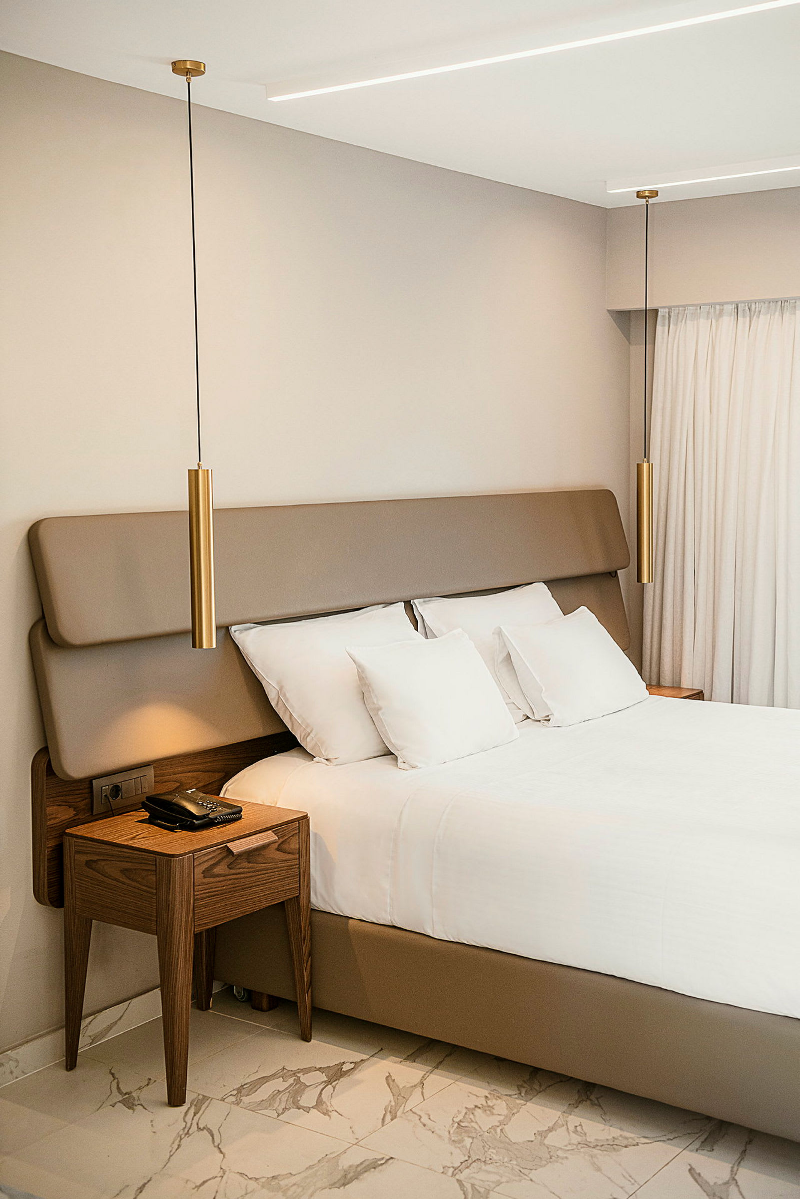 Et moderne og stilrent hotellrom med en seng, trebord og hengende lamper. (AI-generert tekst)