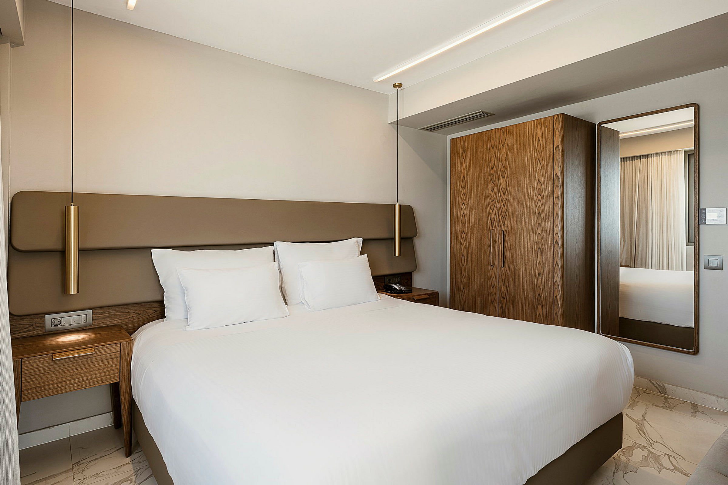 Hotellrom med en stor seng, hvitt sengetøy og tremøbler. (AI-generert tekst)