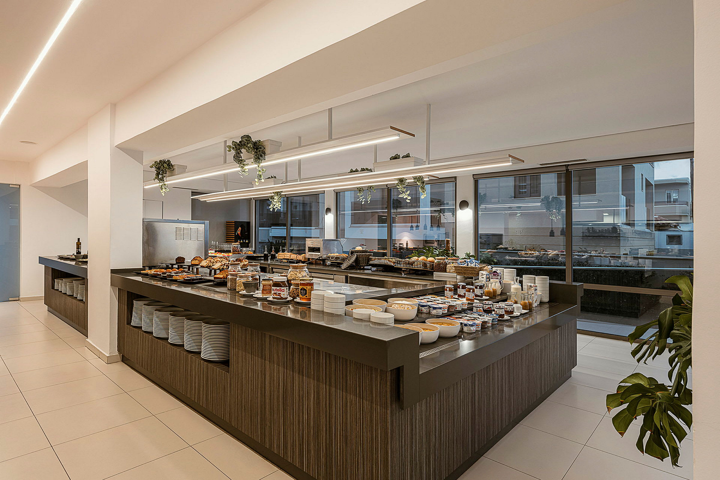 Buffetområde med et utvalg av mat og drikke, inkludert brød, pålegg og skåler, på et moderne serveringsbord i en lys innendørs setting. (AI-generert tekst)
