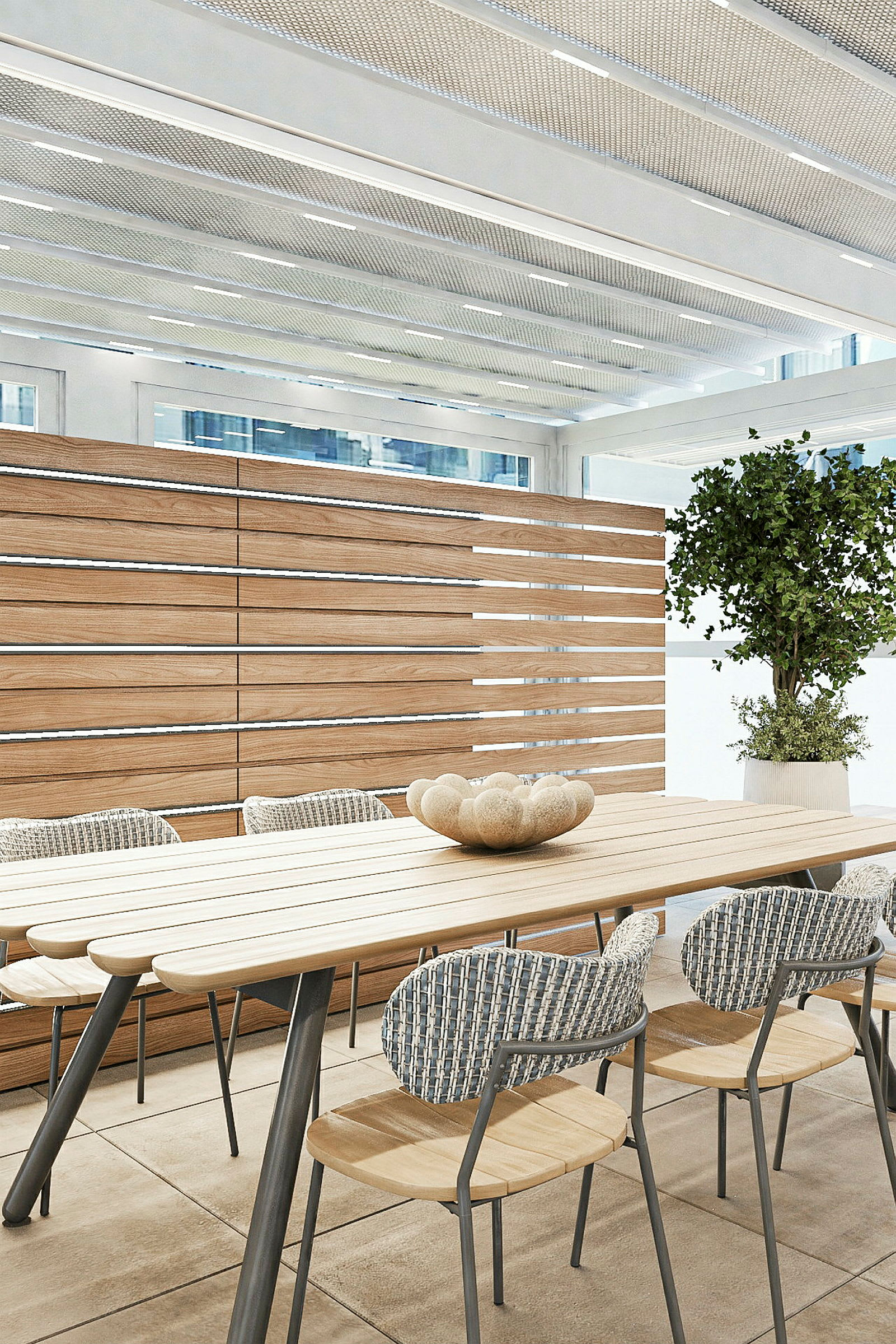 Et moderne rom med bord og stoler i tre, en dekorativ skål på bordet og en stor plante i siden, omgitt av glass og paneler i tre. (AI-generert tekst)