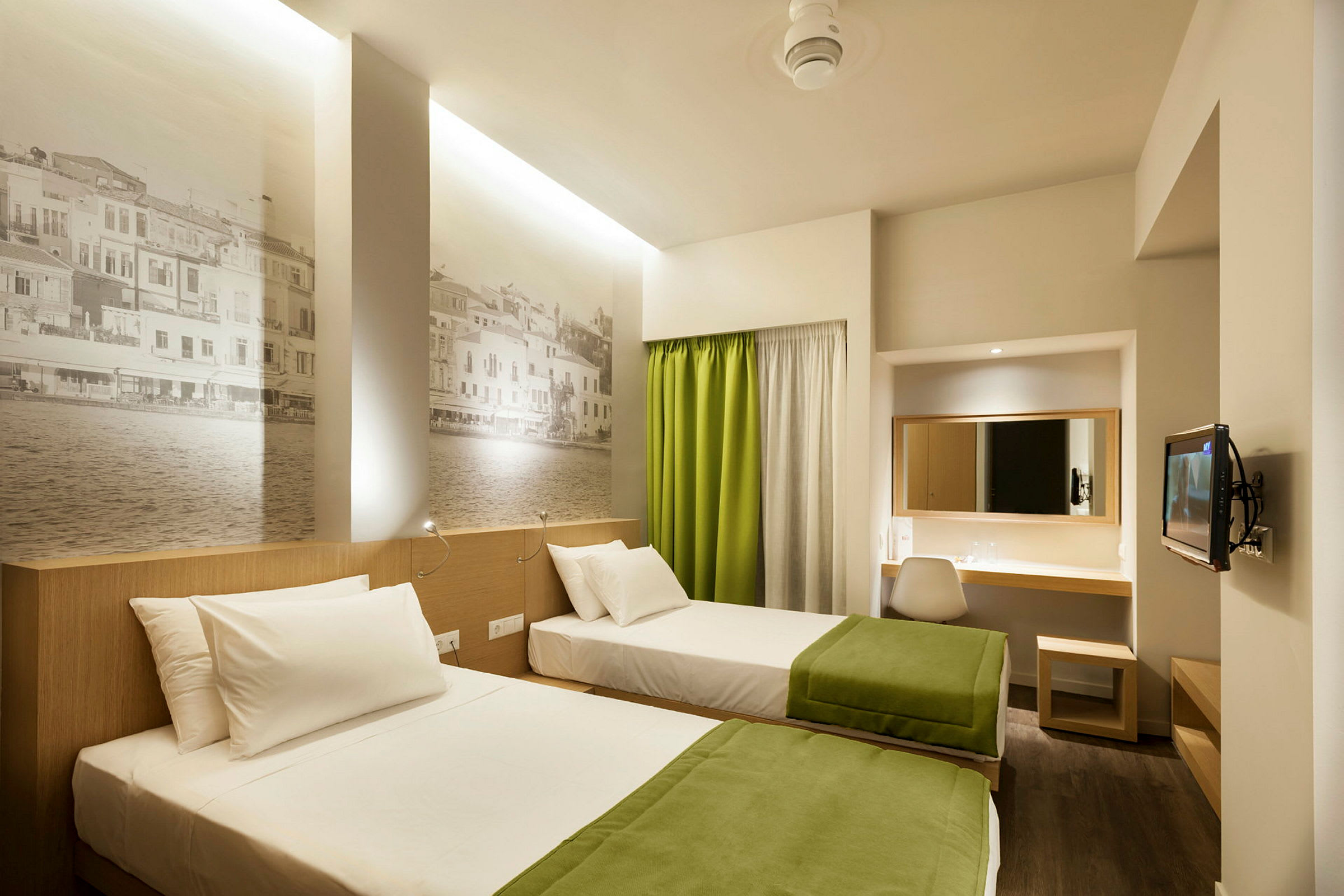 To enkeltsenger med grønne tepper i et moderne hotellrom med veggmalerier og skrivebord. (AI-generert tekst)