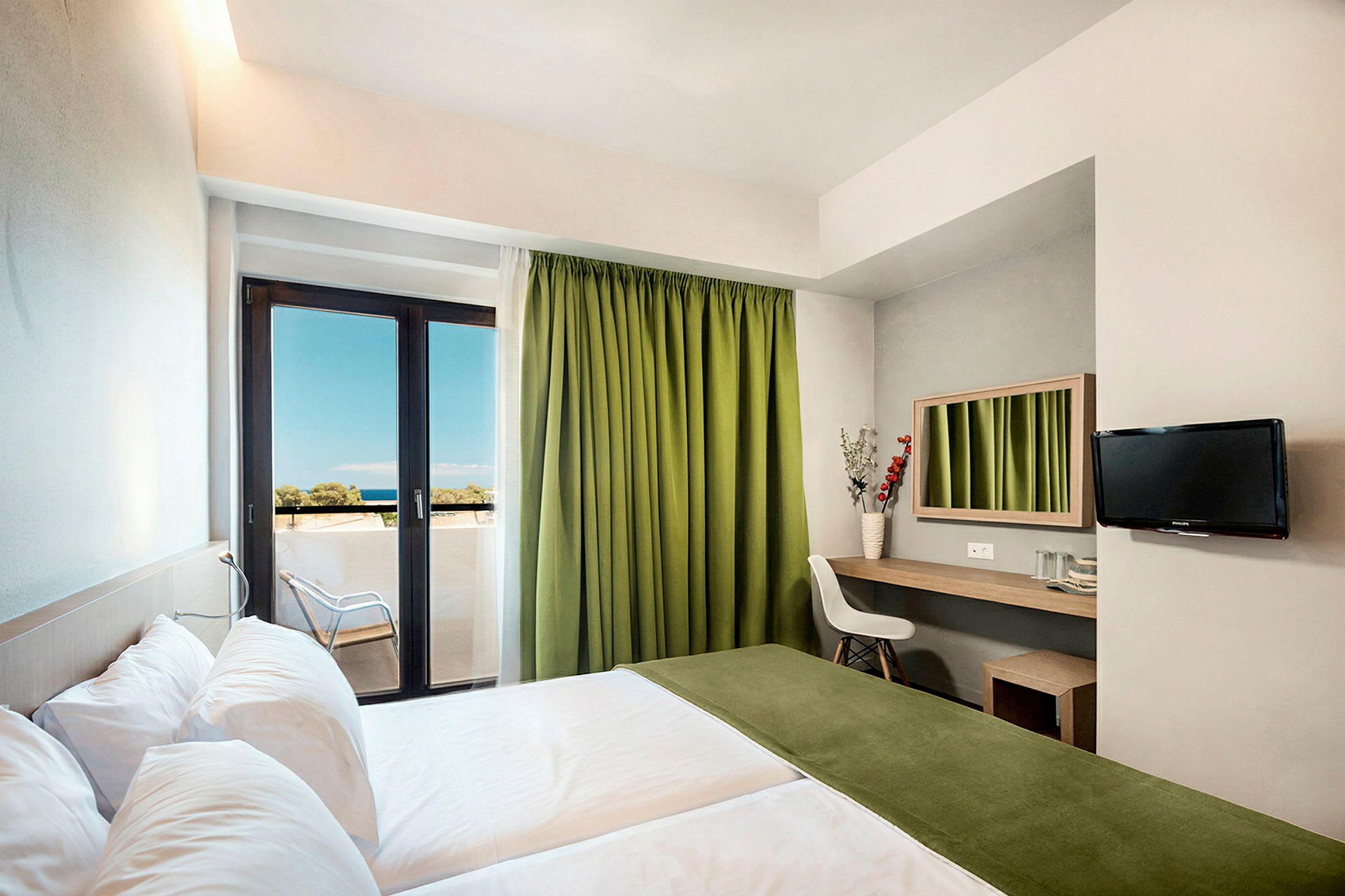 Et hotellrom med to senger, en arbeidsflate med speil, en stol og en TV på veggen. Rommet har en balkong med grønne gardiner og utsikt mot havet. (AI-generert tekst)