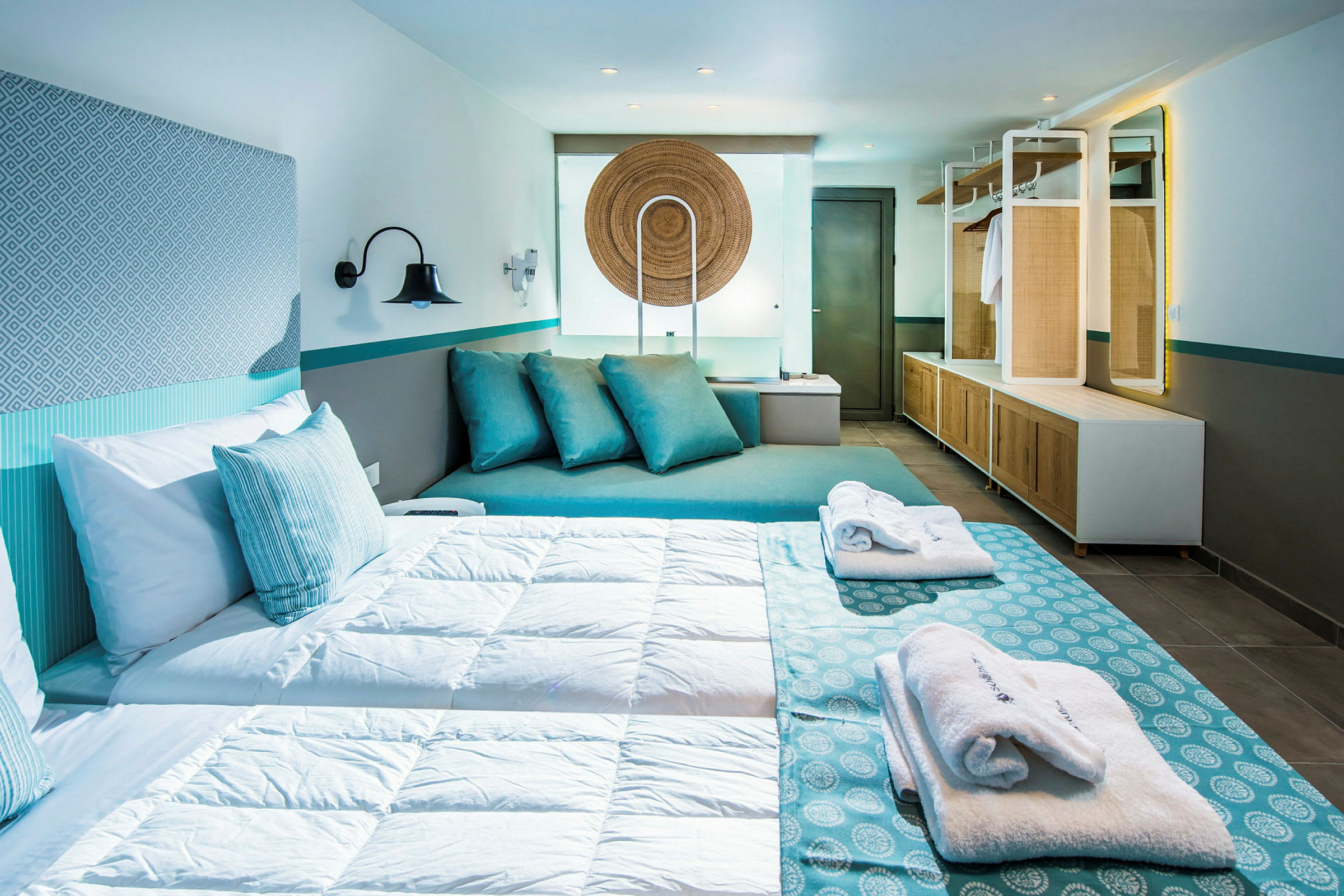 Et moderne hotellrom med en dobbeltseng, dekorert i blå og hvite farger, sitteområde med puter og garderobe. (AI-generert tekst)