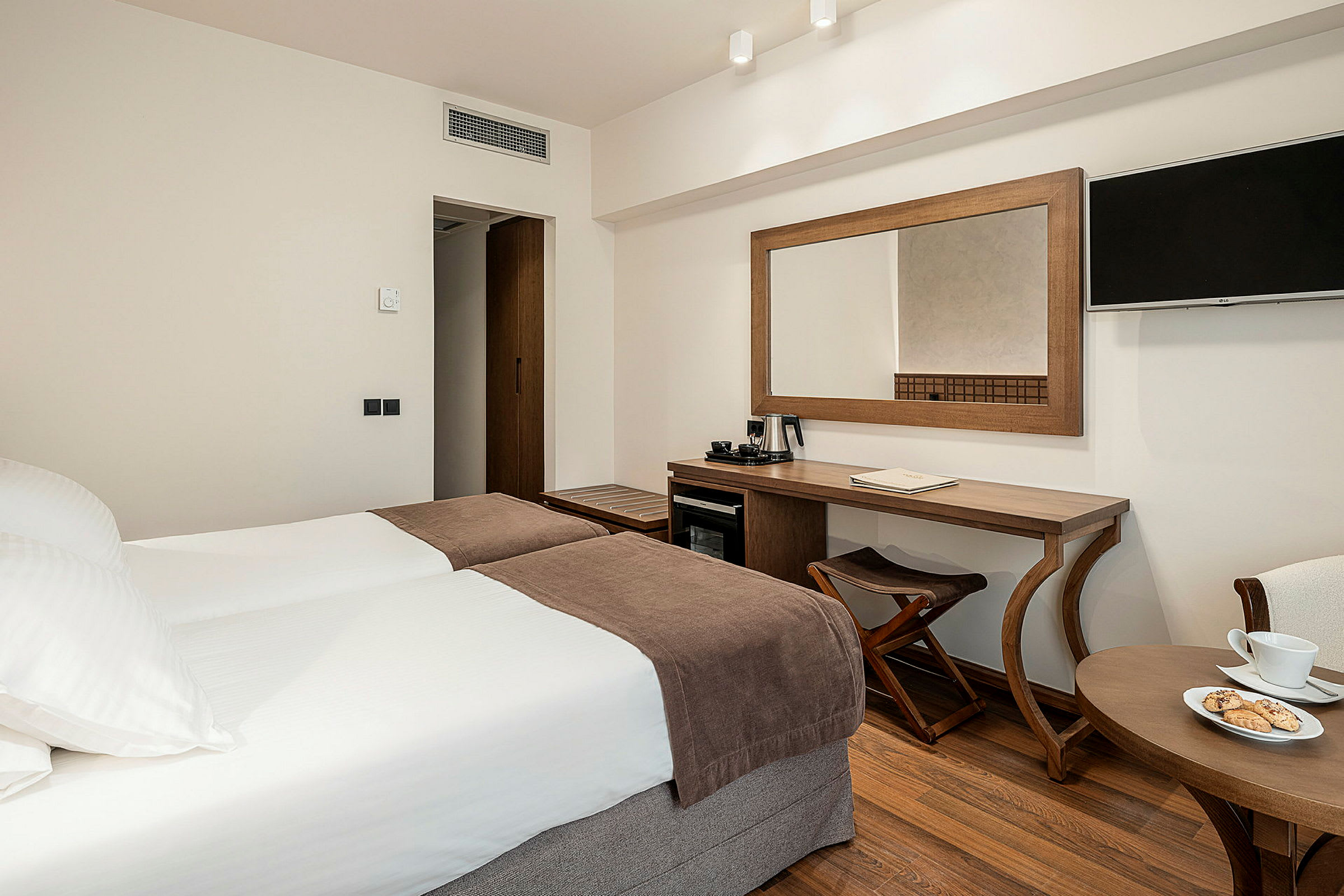 Hotellrom med to enkeltsenger, skrivebord, veggmontert TV og en kaffetrakter. (AI-generert tekst)