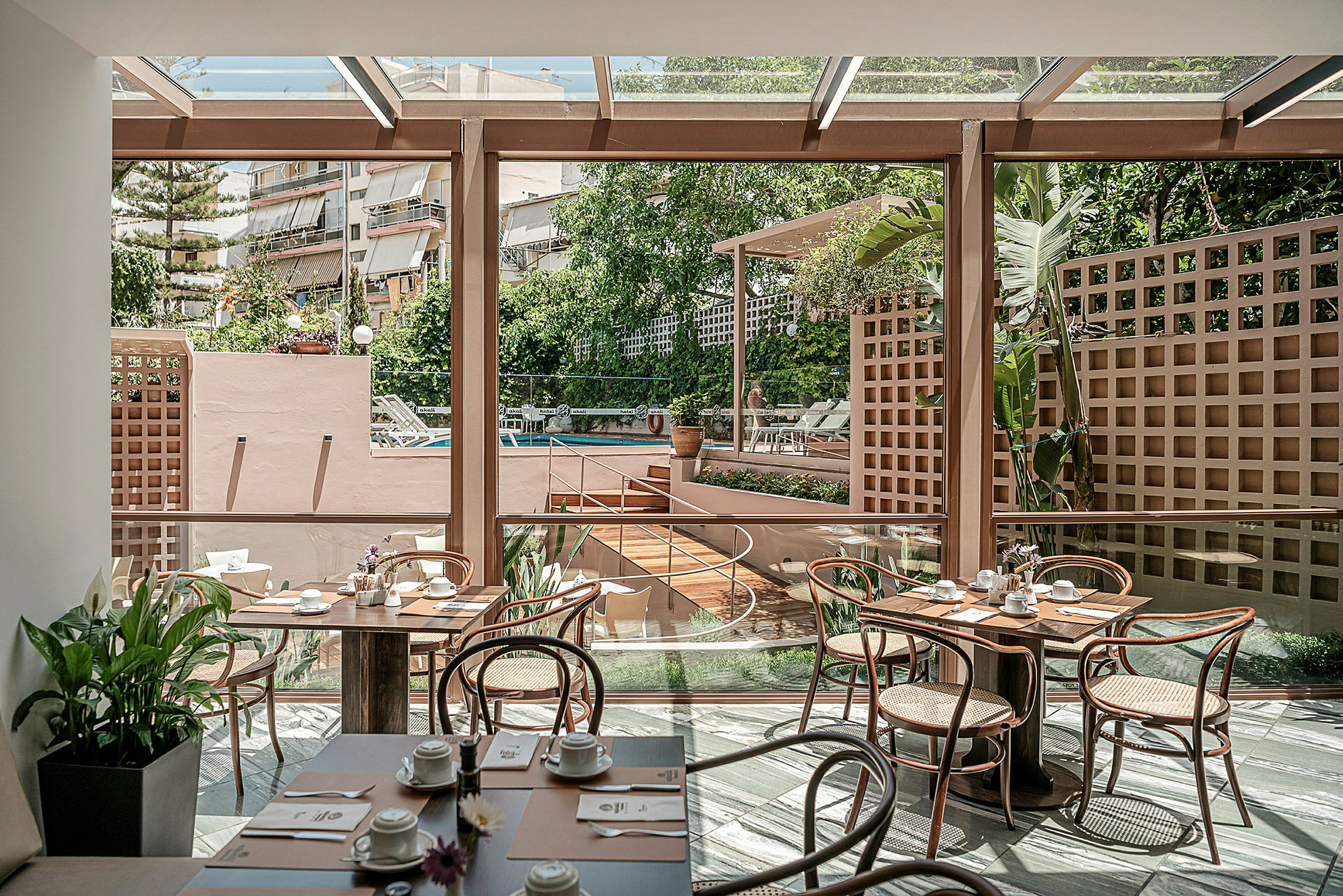 Interiør av en lys restaurant med glassvegger og utsikt mot et utendørs bassengområde. (AI-generert tekst)