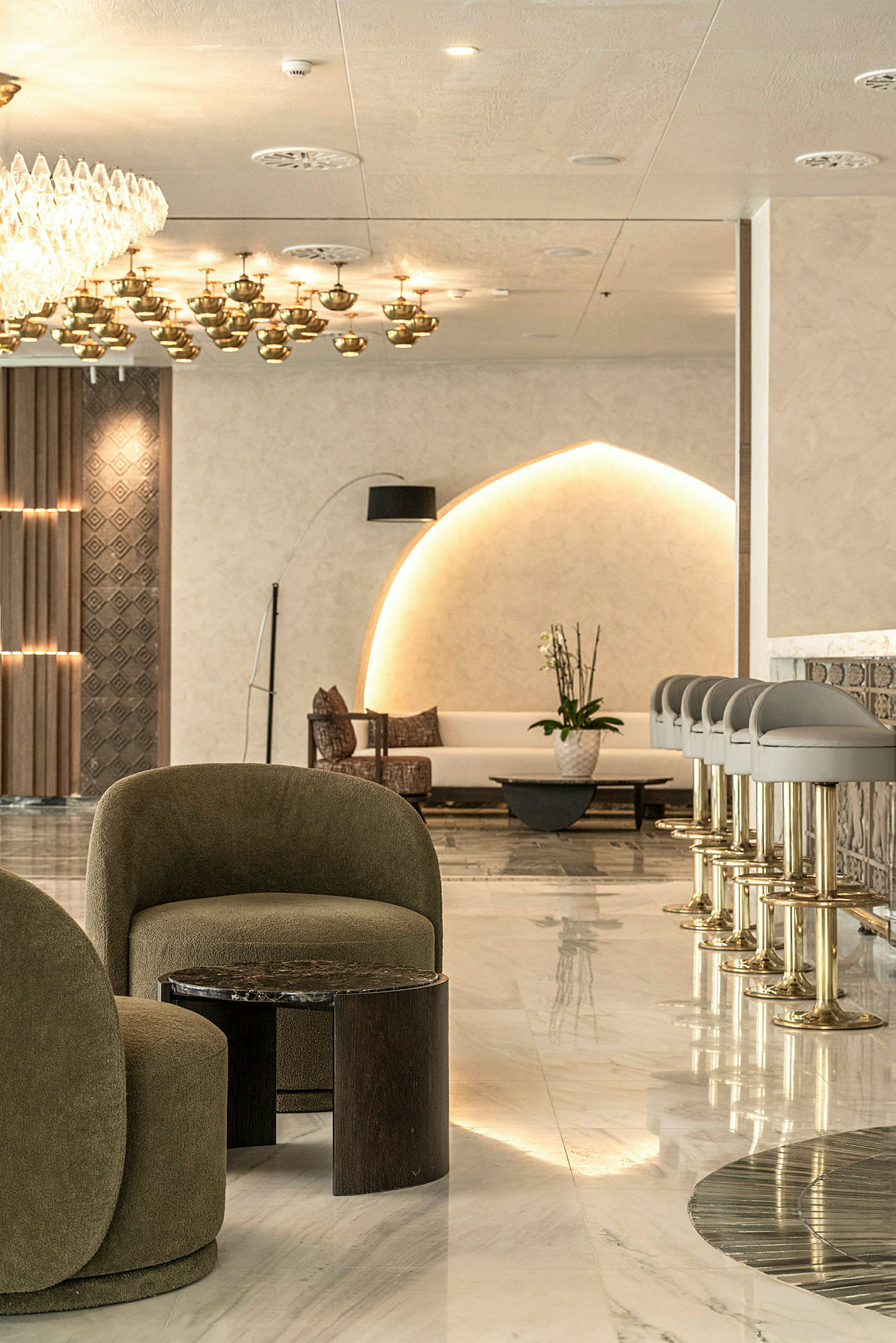 En elegant hotellobby med moderne møbler, inkludert grønne lenestoler og en rad med barkrakker. (AI-generert tekst)